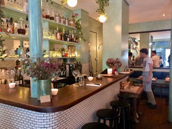 Modern bistro interior with well-stocked bar, tiled walls, and plants adding natural decor.