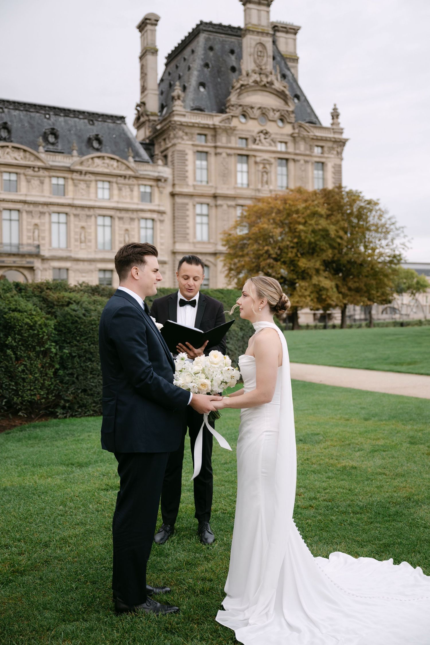Couple shares intimate wedding ceremony moment on the lawn of an elegant French chateau with historic architecture.
