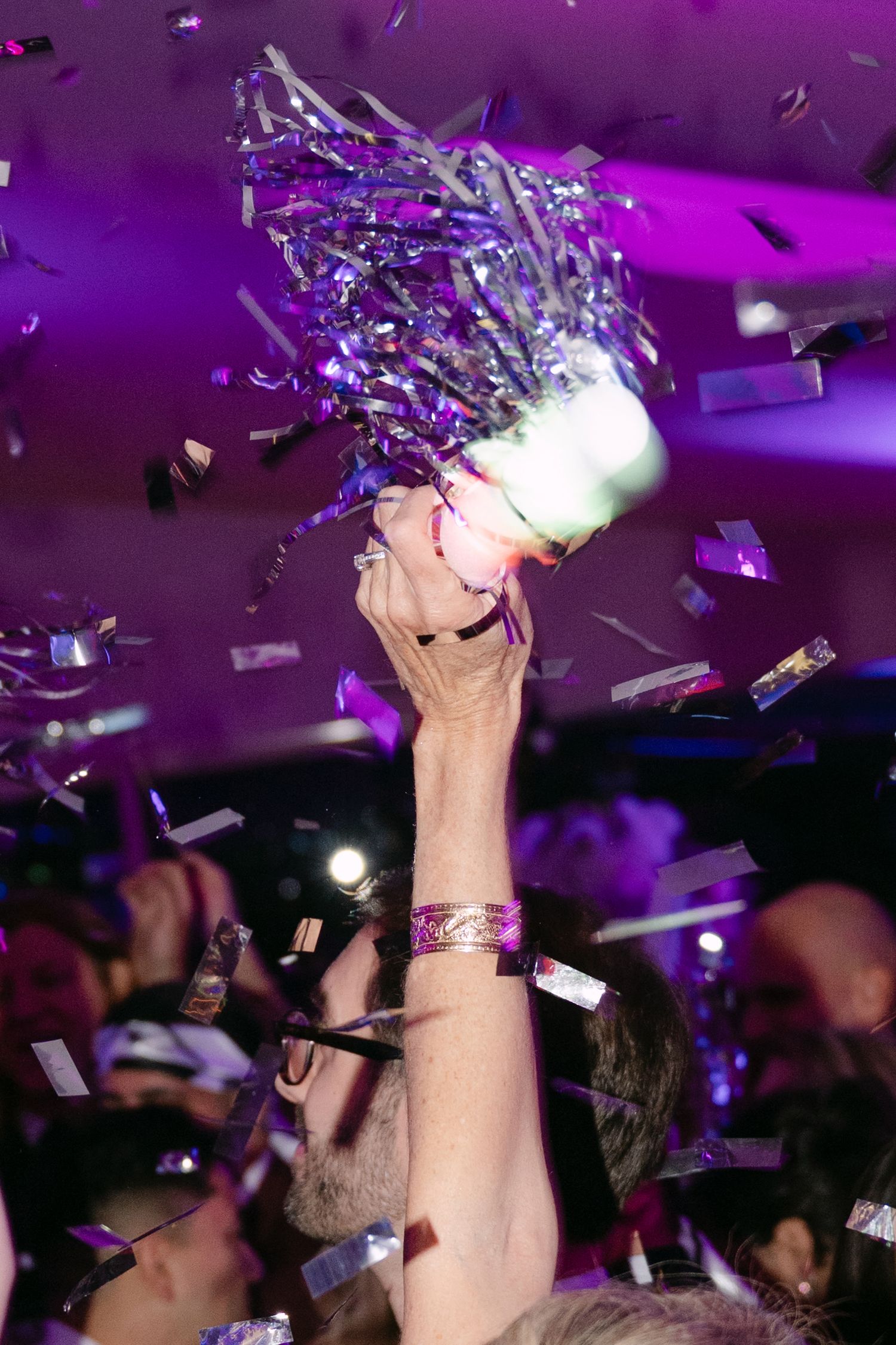 Hand tossing silver confetti and streamers at vibrant purple-lit celebration party.