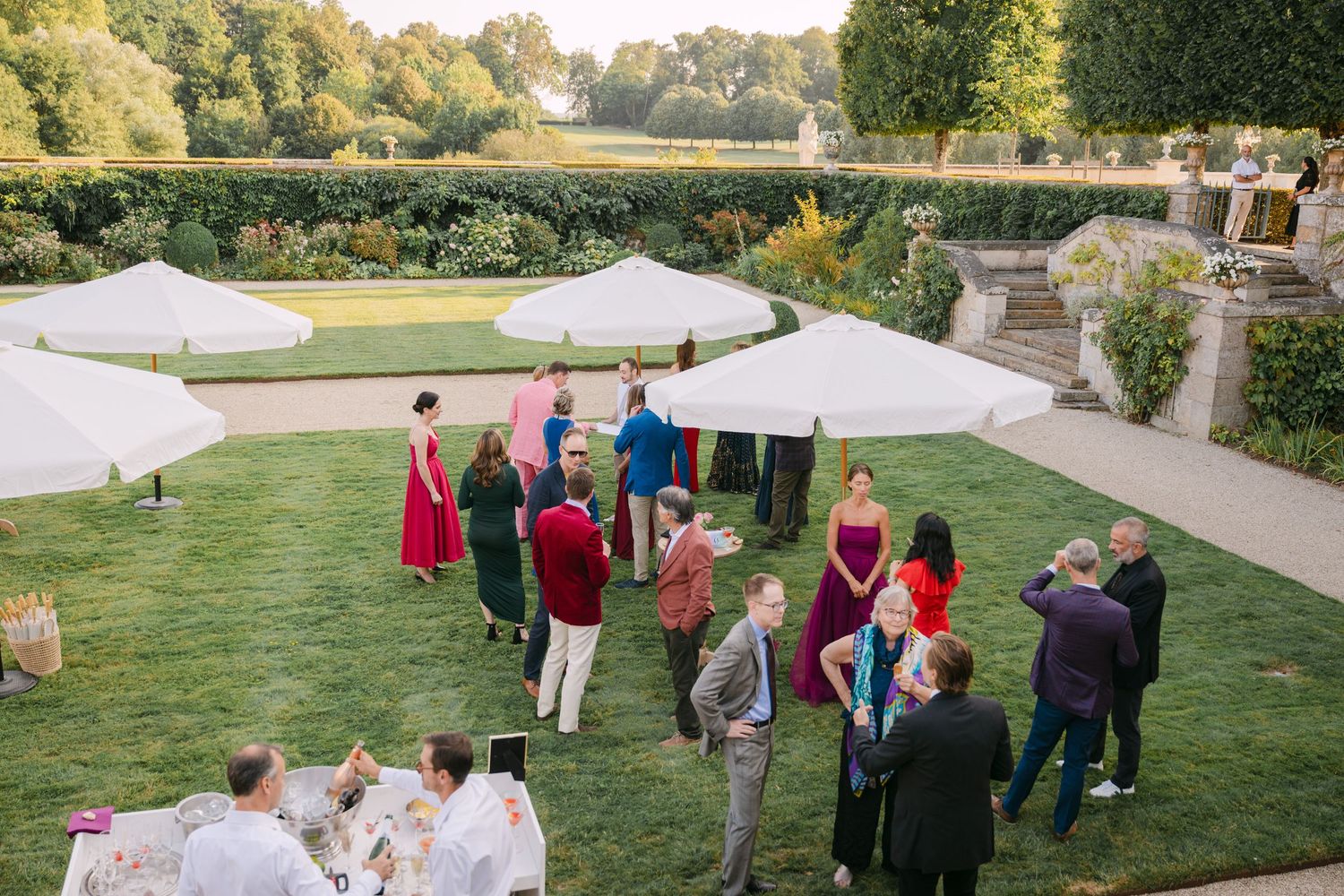 Outdoor wedding cocktail hour with guests mingling on a manicured lawn beneath large white market umbrellas.
