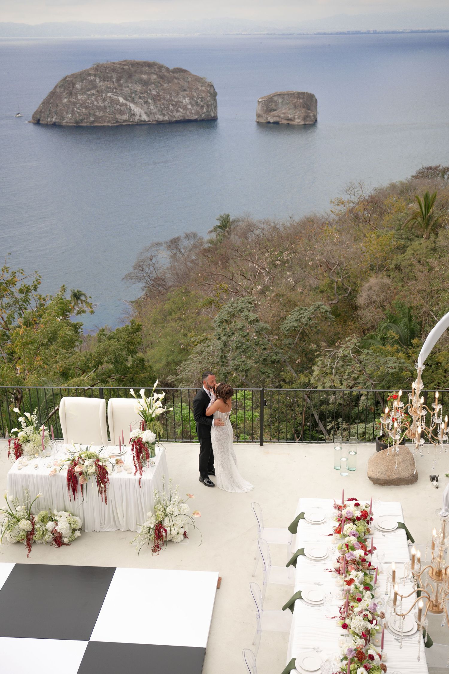 Bride and groom share first dance on terrace overlooking ocean with rocky islands.