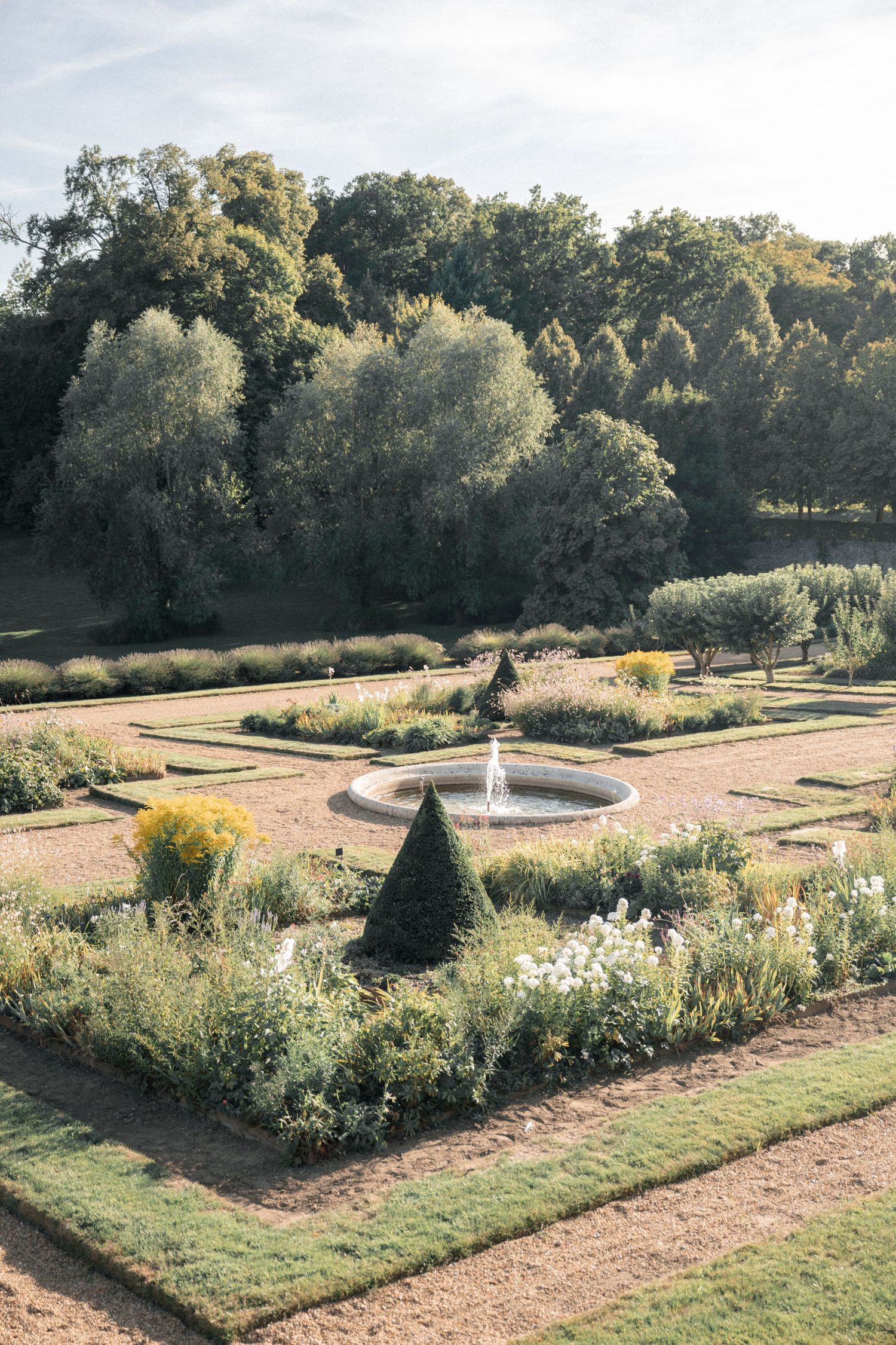Formal French garden with geometric hedges, fountain centerpiece and mature trees.