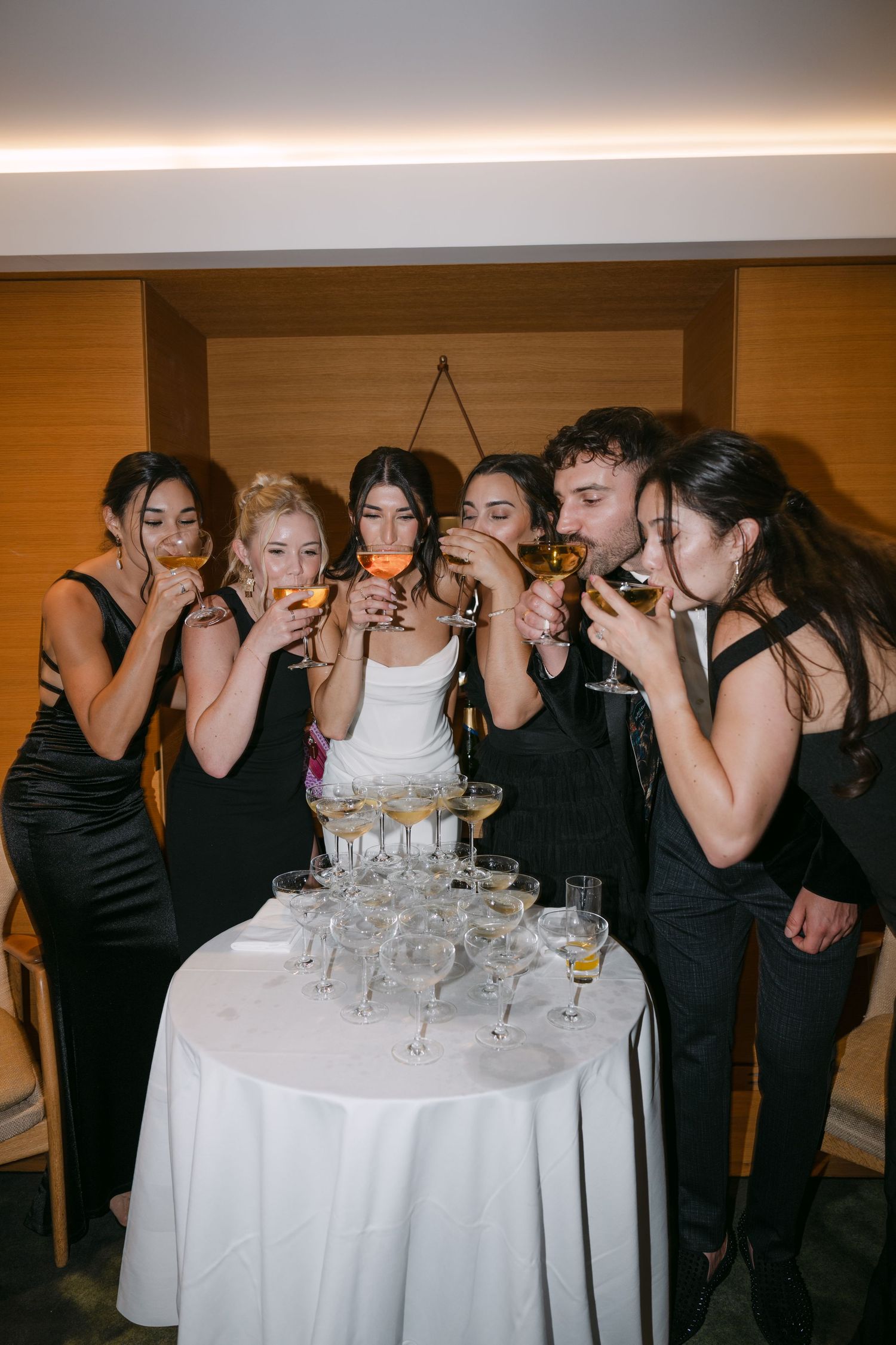 Wedding party in black and white attire toasting champagne glasses at reception.