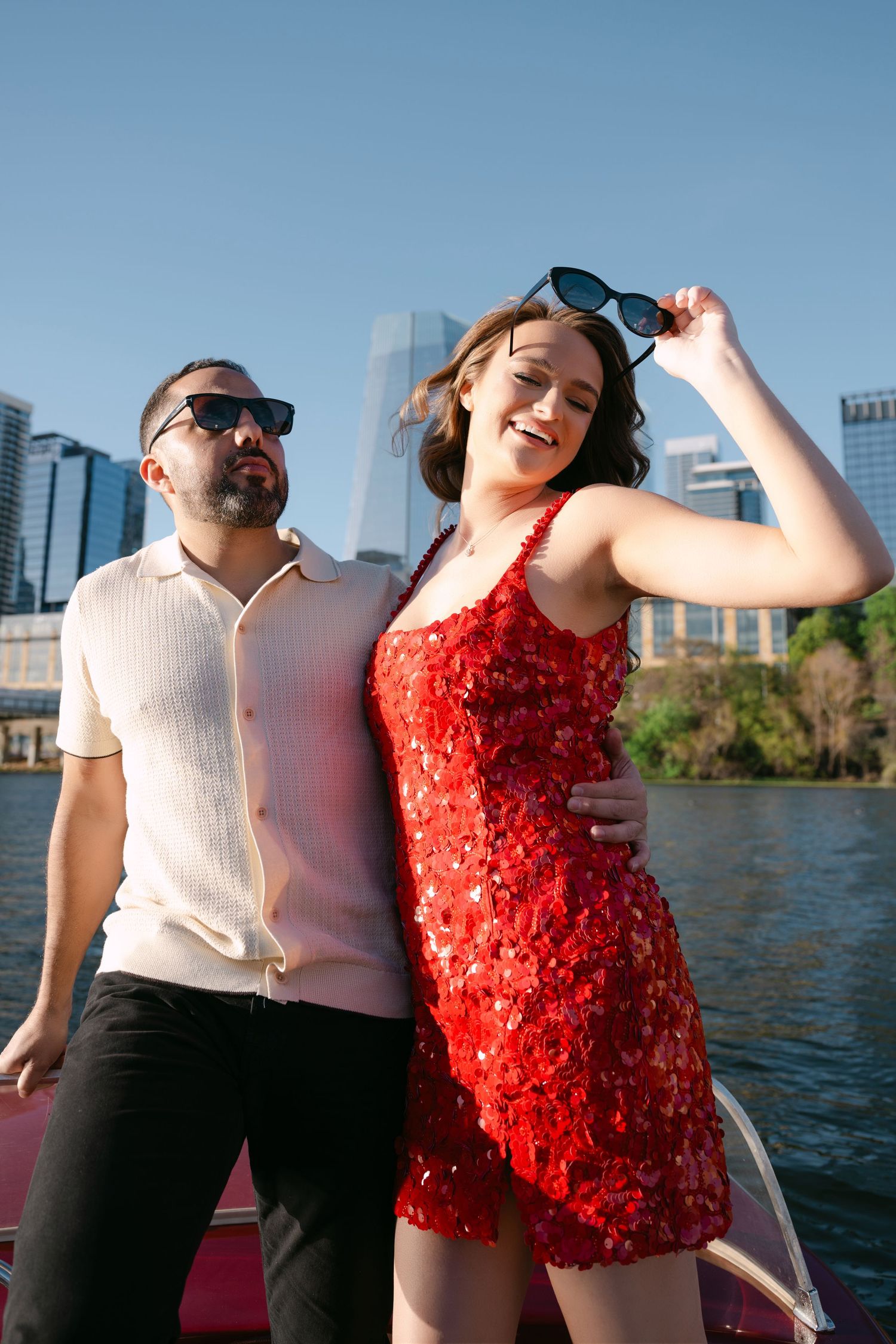 Couple in sunglasses posing on a boat with Austin city skyline in the background.