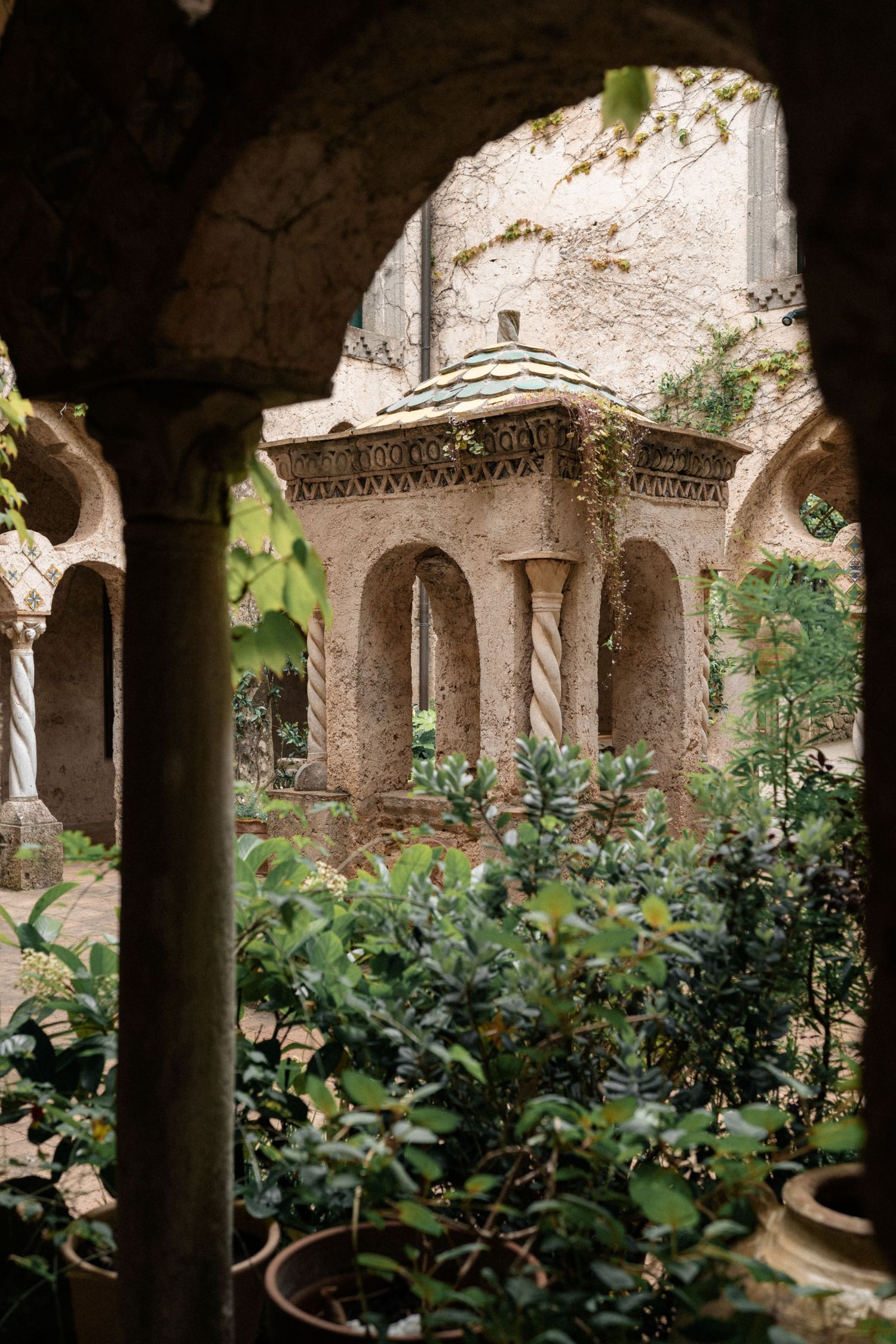Ancient cloister courtyard with twisted columns, arches, and lush greenery in Italian monastery.