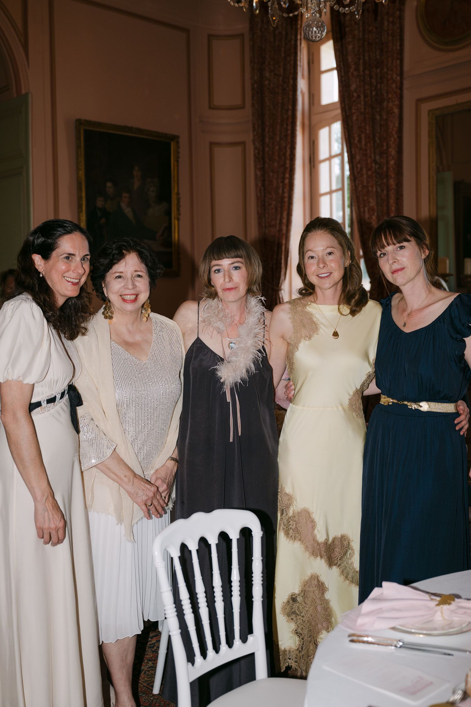 Five elegantly dressed women posing together in a ornate French chateau dining room.
