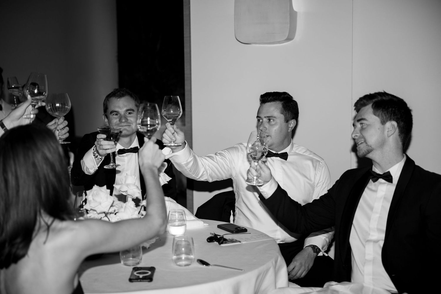 Black and white photo of men in tuxedos raising champagne glasses in a toast.