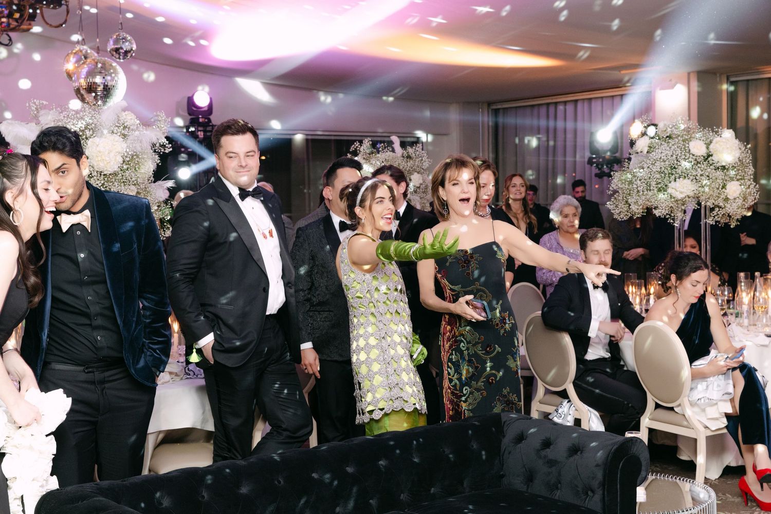 Excited wedding guests celebrating on dance floor with confetti falling at elegant reception.