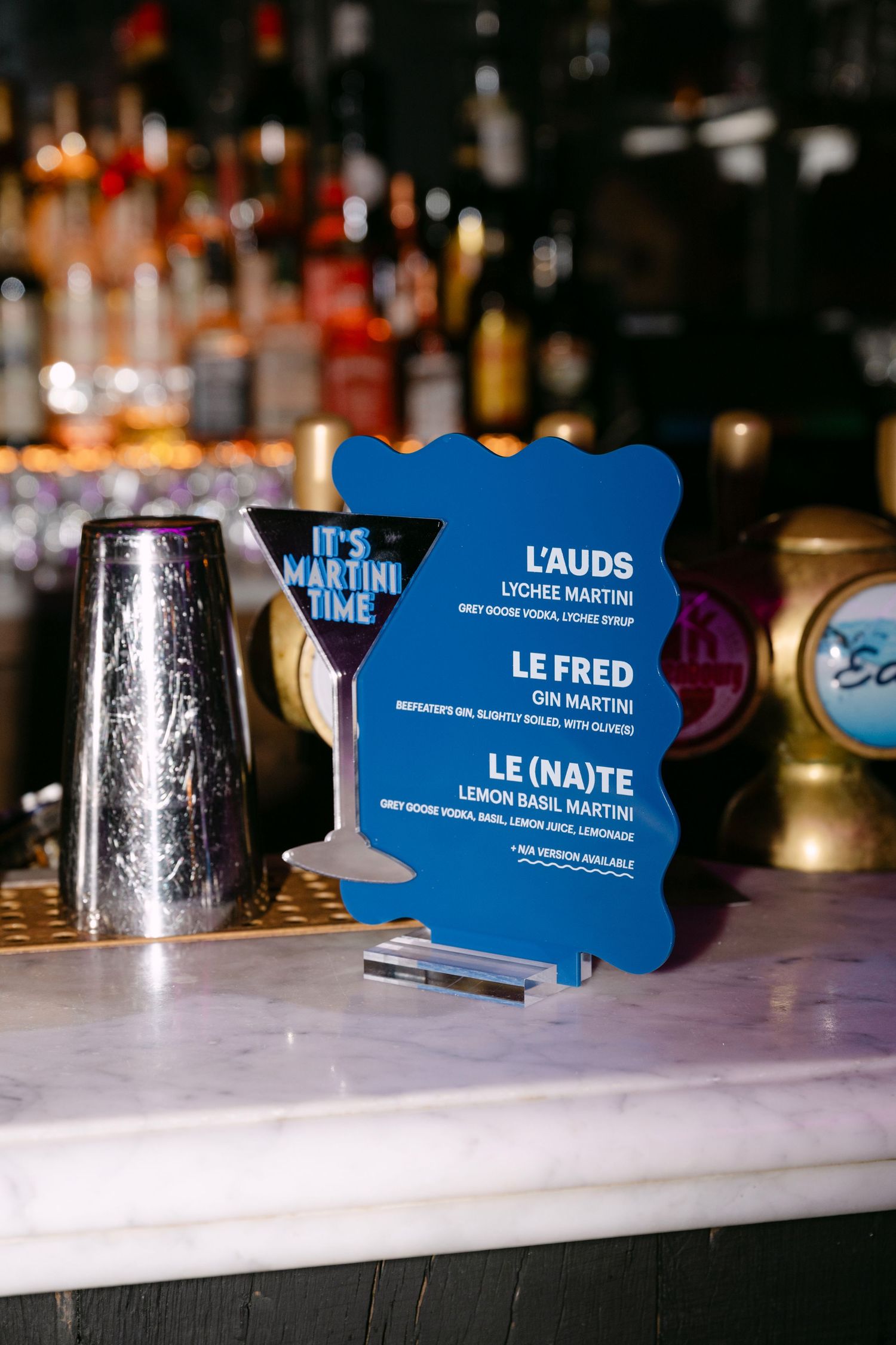 Blue martini-shaped cocktail menu sign featuring signature drinks at a wedding bar.
