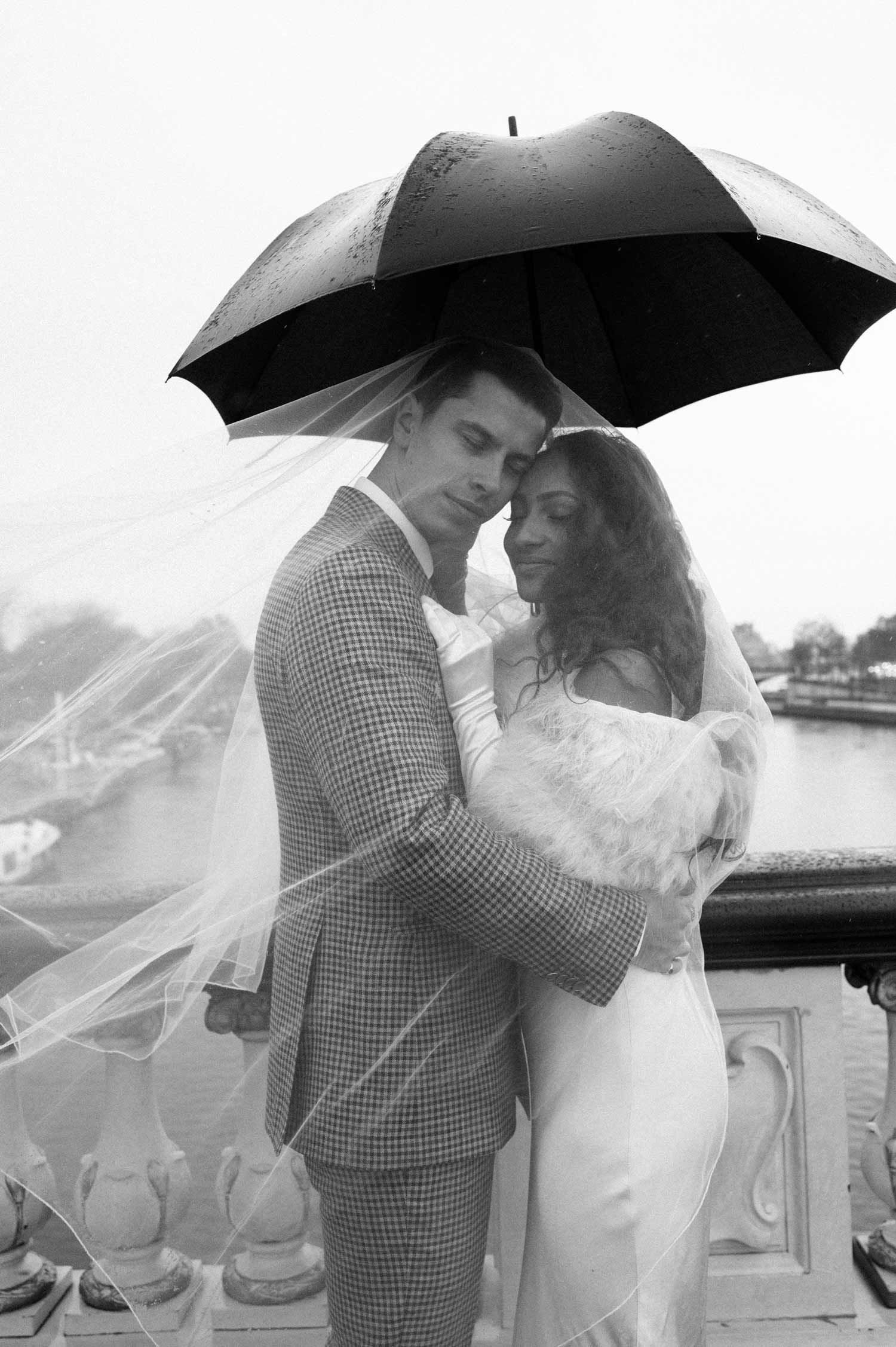 A black and white wedding portrait featuring a couple sharing an intimate moment under an umbrella.