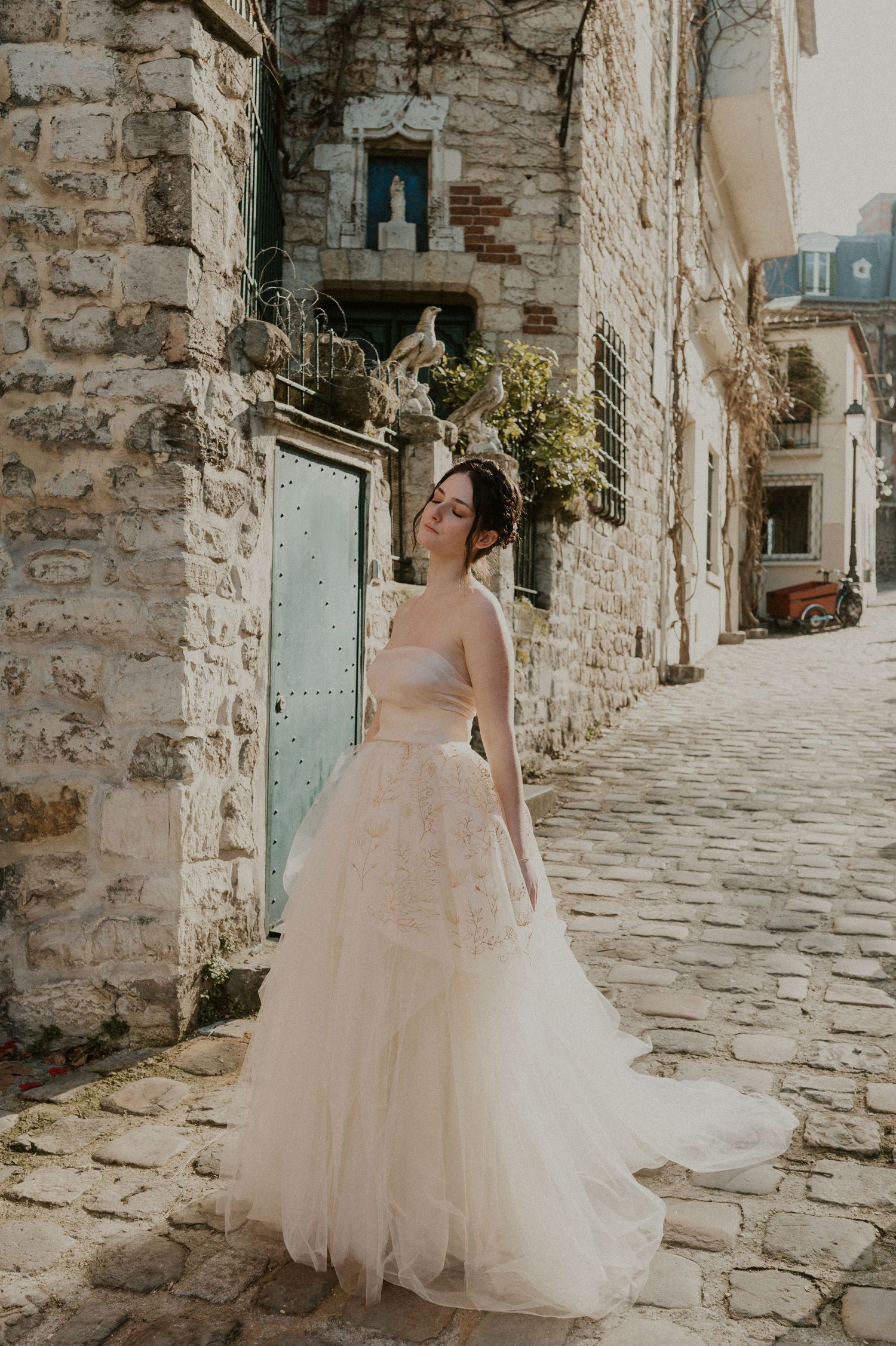 Bridal portrait in a flowing tulle gown against rustic stone walls and cobblestone street.