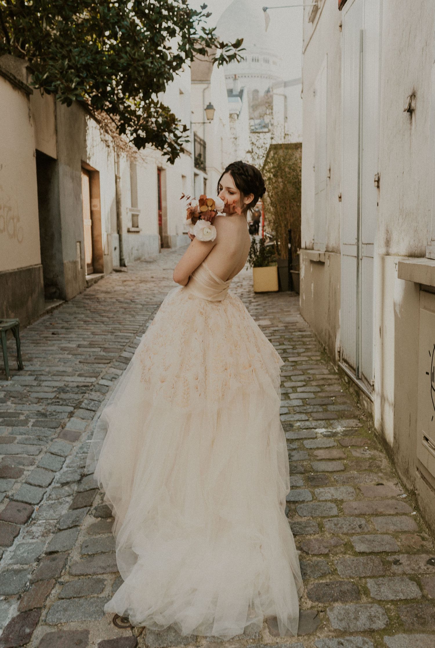 A bride in a flowing tulle gown glances over her shoulder in a charming European alleyway.