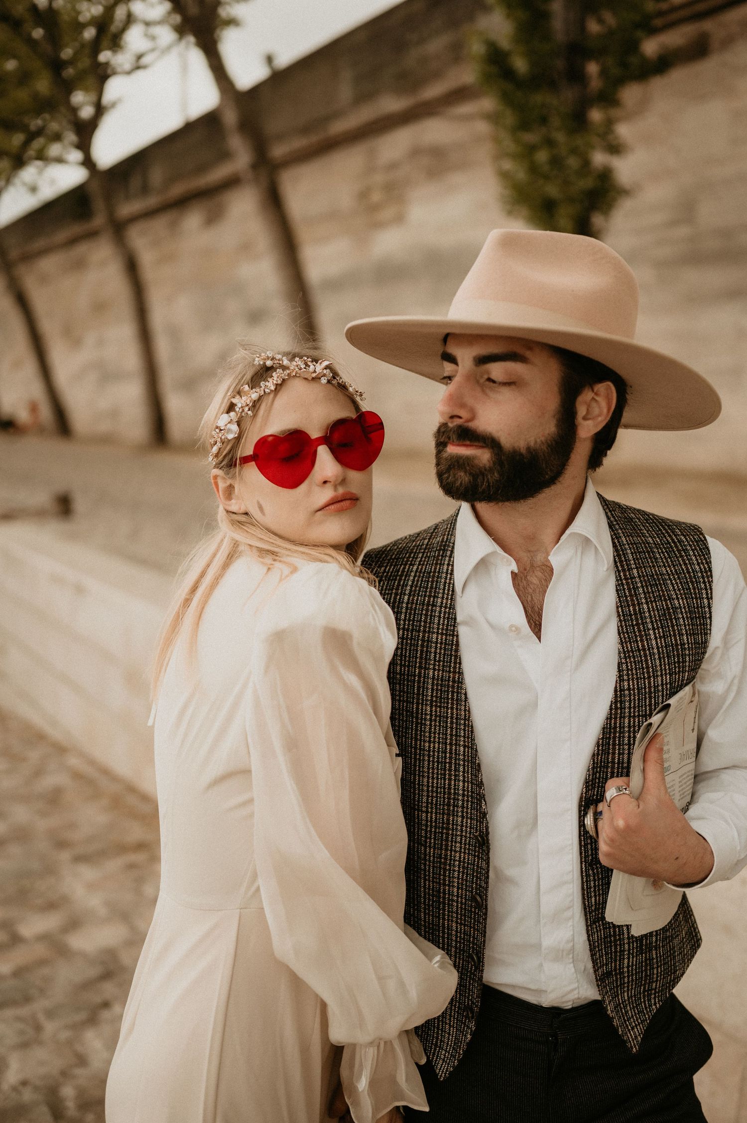 A vintage-inspired wedding portrait featuring heart-shaped sunglasses and a wide-brimmed hat.