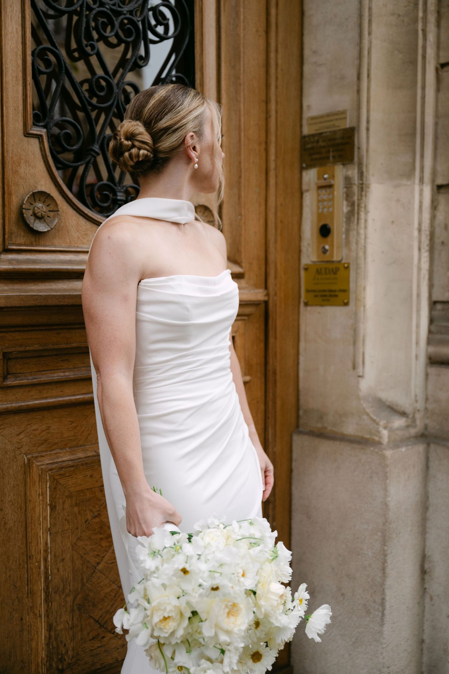 A bride in a white wedding dress holds an elegant bouquet of white orchids against an ornate wooden door backdrop.