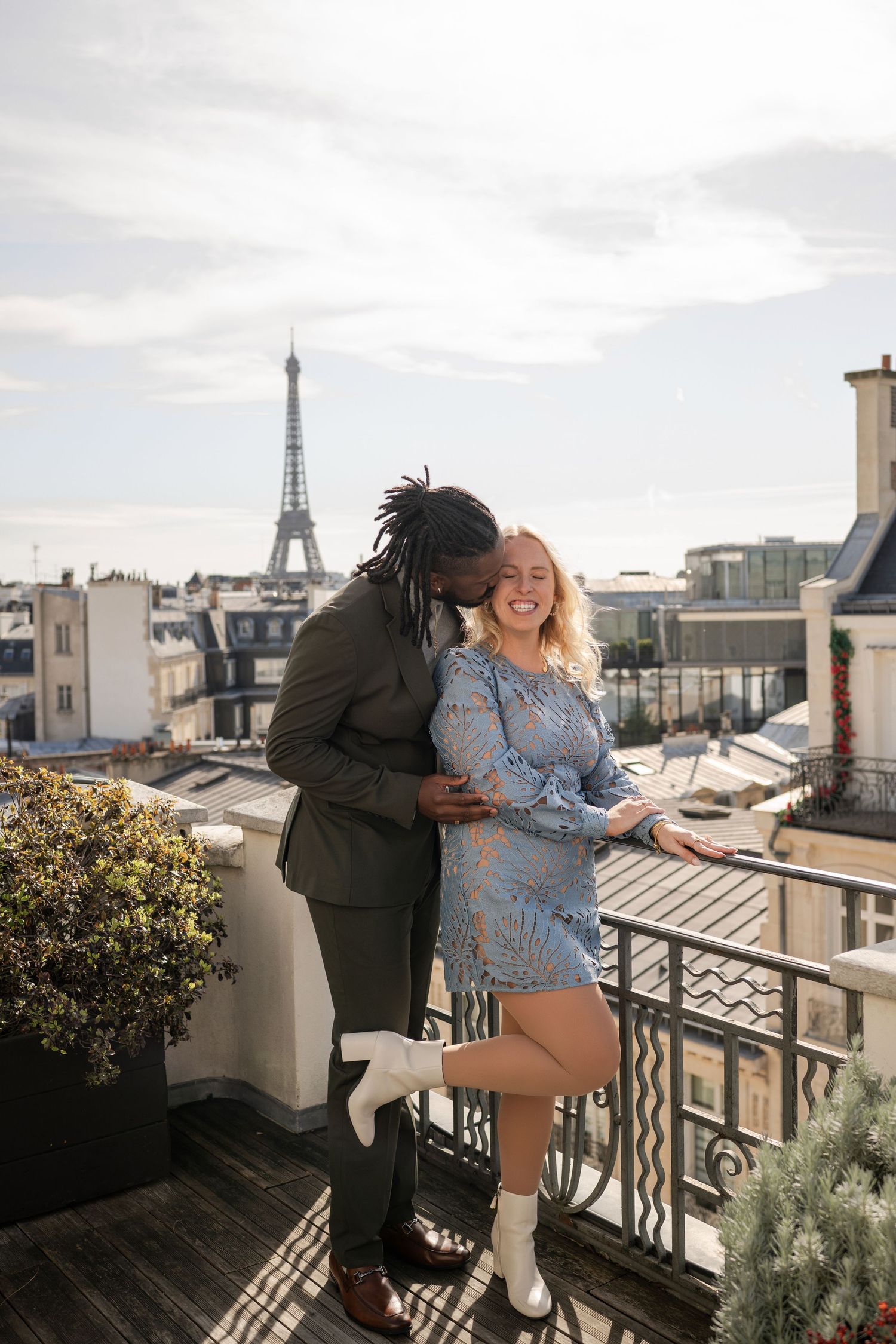 Couple embracing on a Parisian rooftop terrace with the Eiffel Tower in the background on a sunny day.