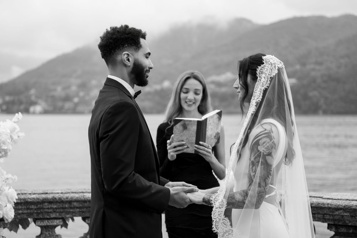 Black and white photo of bride and groom holding hands during wedding ceremony by Lake Como.