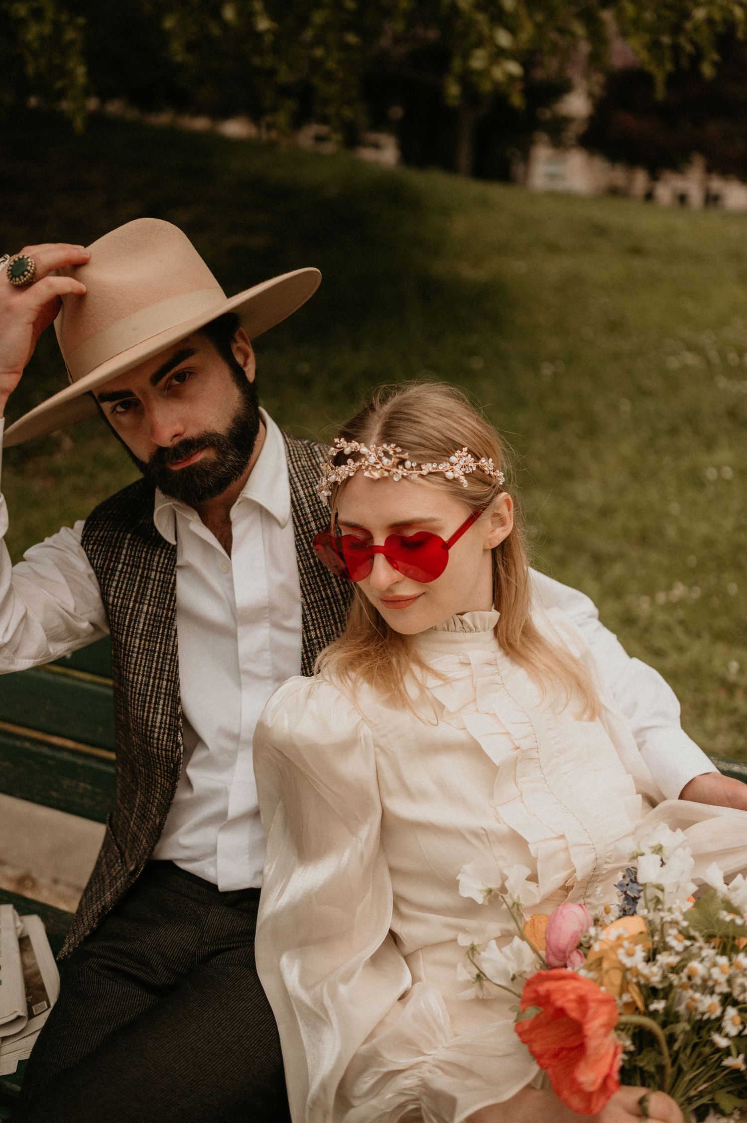 An intimate portrait of a couple on a park bench wearing vintage attire and heart-shaped glasses.
