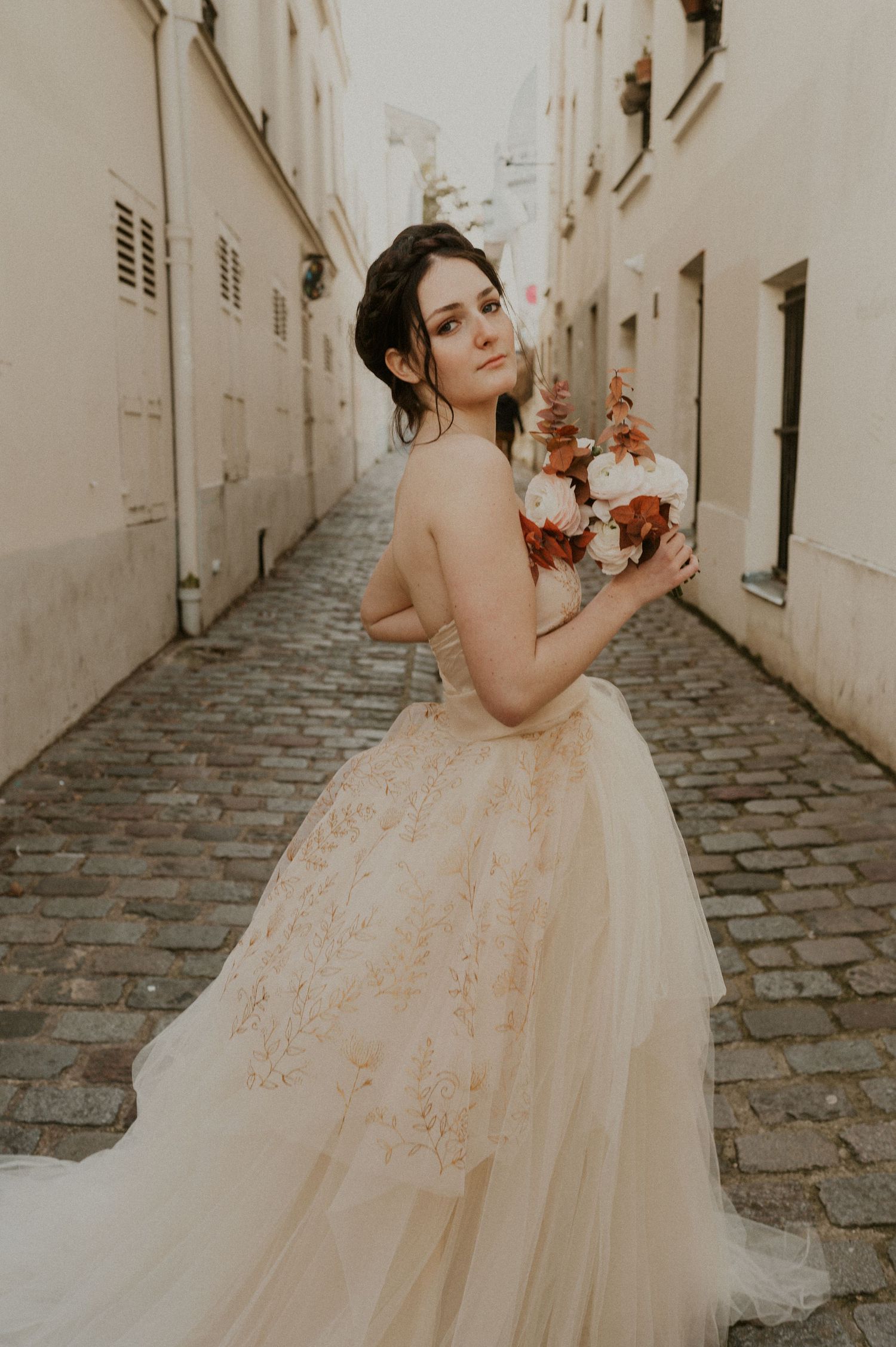 Romantic bridal portrait with autumn bouquet against white stone walls on cobblestone street.