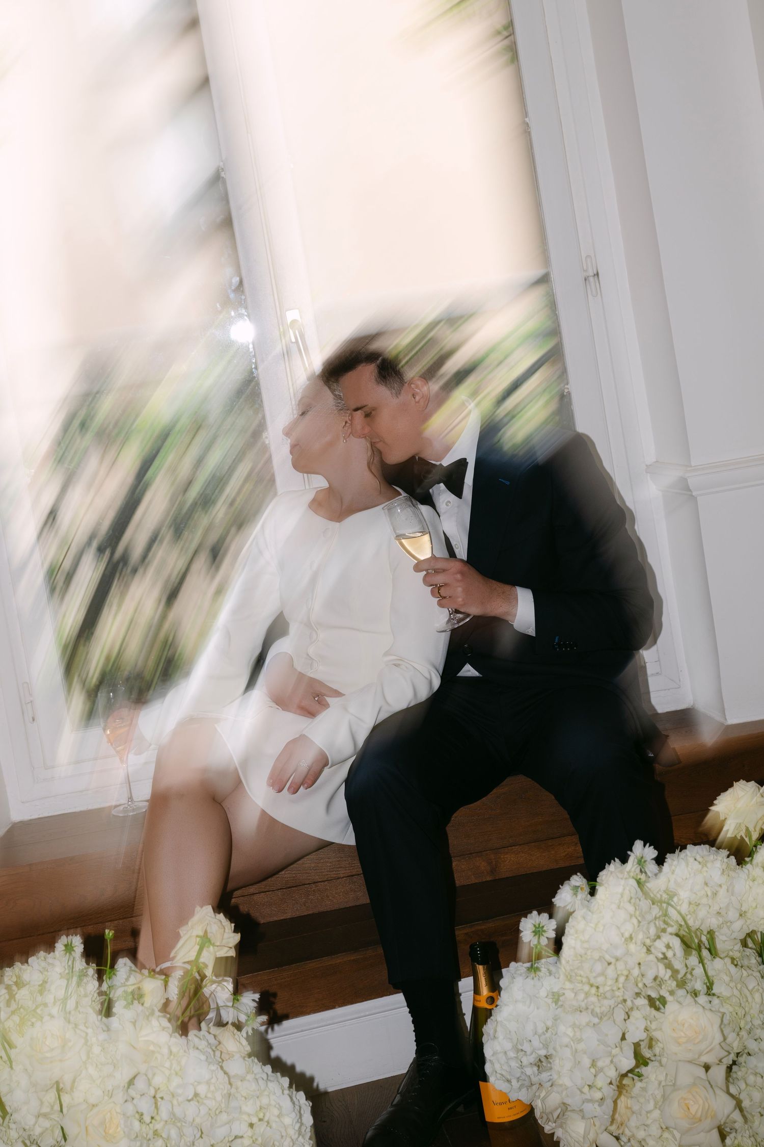 A bride and groom share an intimate moment in a motion-blurred wedding photo with white floral arrangements.