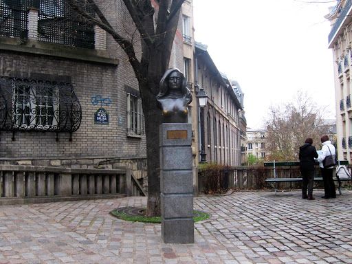 Bronze bust monument on cobblestone street corner in historic Paris neighborhood.