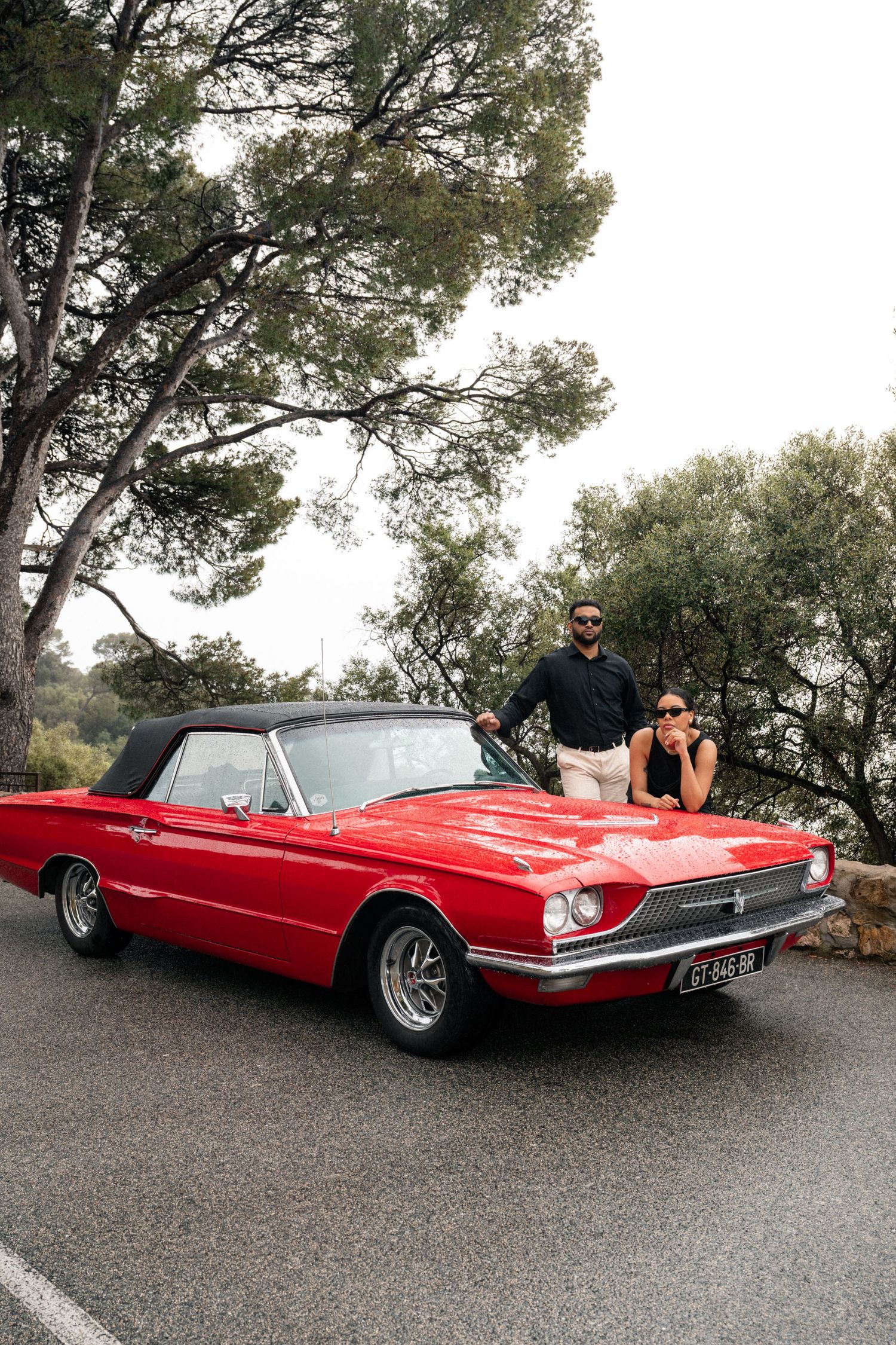 Affectionate couple wearing sunglasses sits in a vintage red car, creating a stylish and romantic mood.