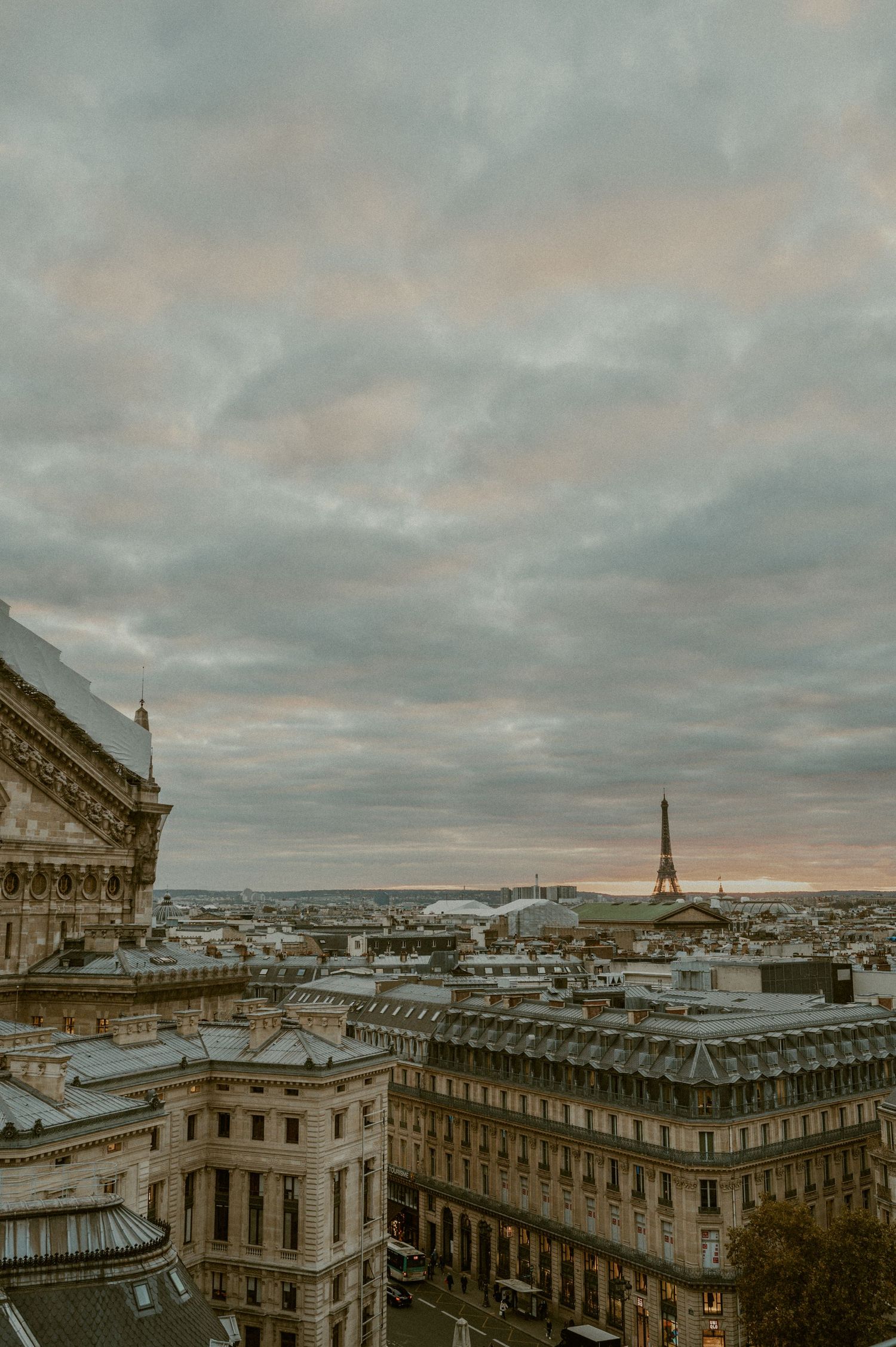 Panoramic view of Paris skyline at sunset with the Eiffel Tower visible in the distance among historic buildings.