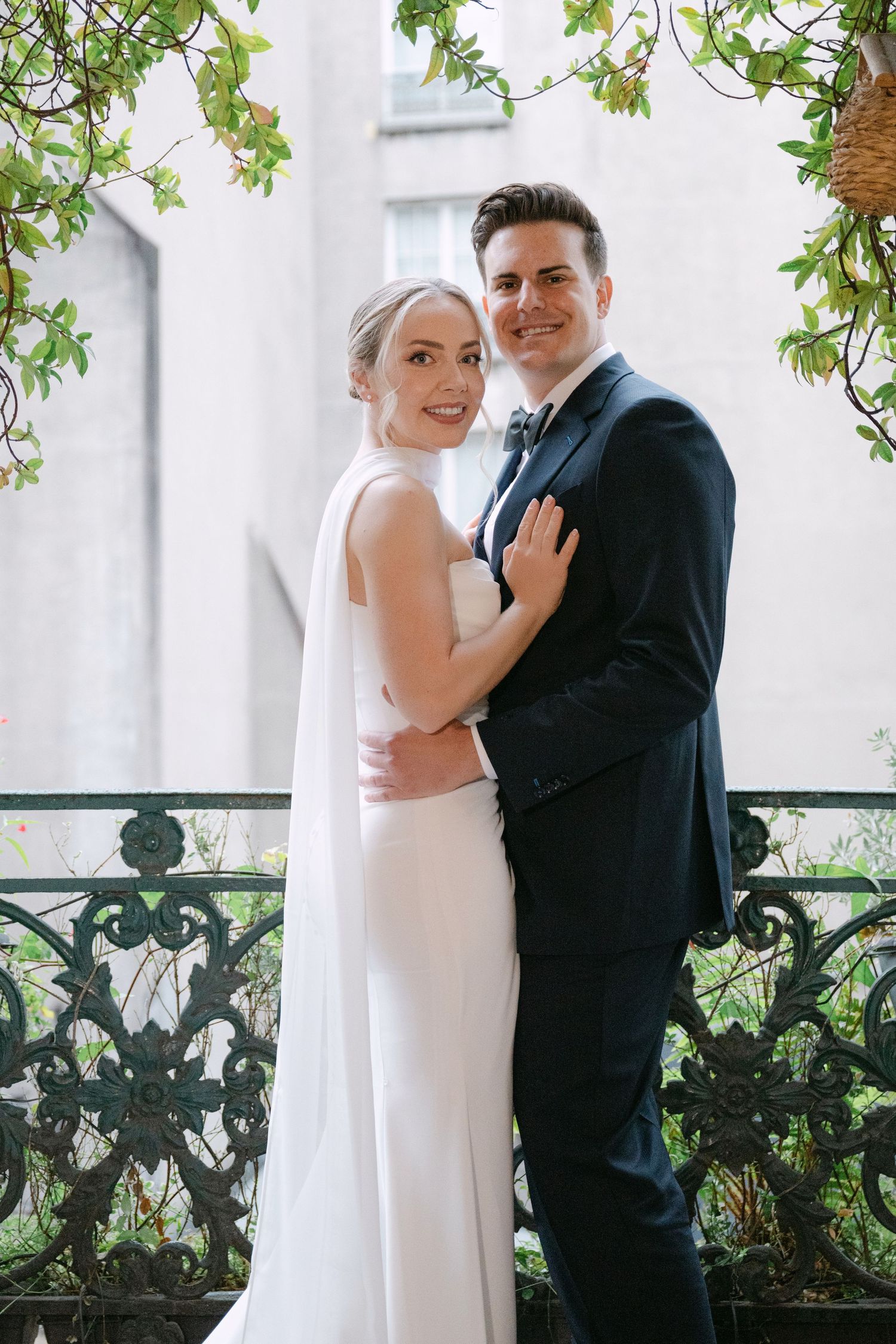Elegant couple posing on a balcony with greenery and white architectural details.