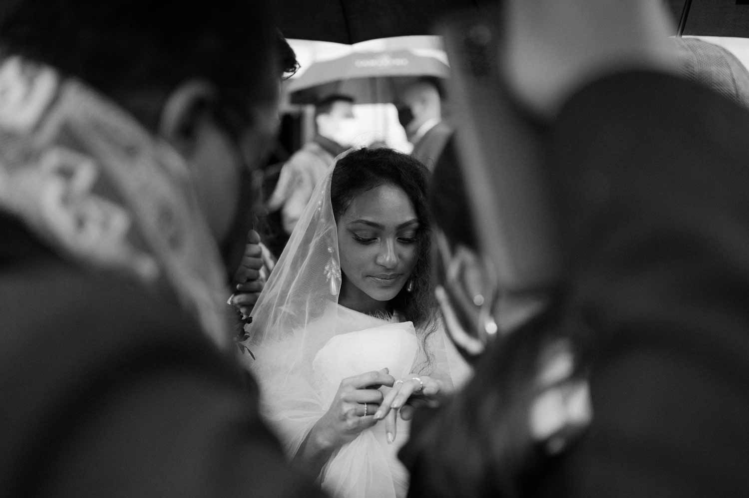 A black and white photo of a bride surrounded by guests during an intimate wedding ceremony.