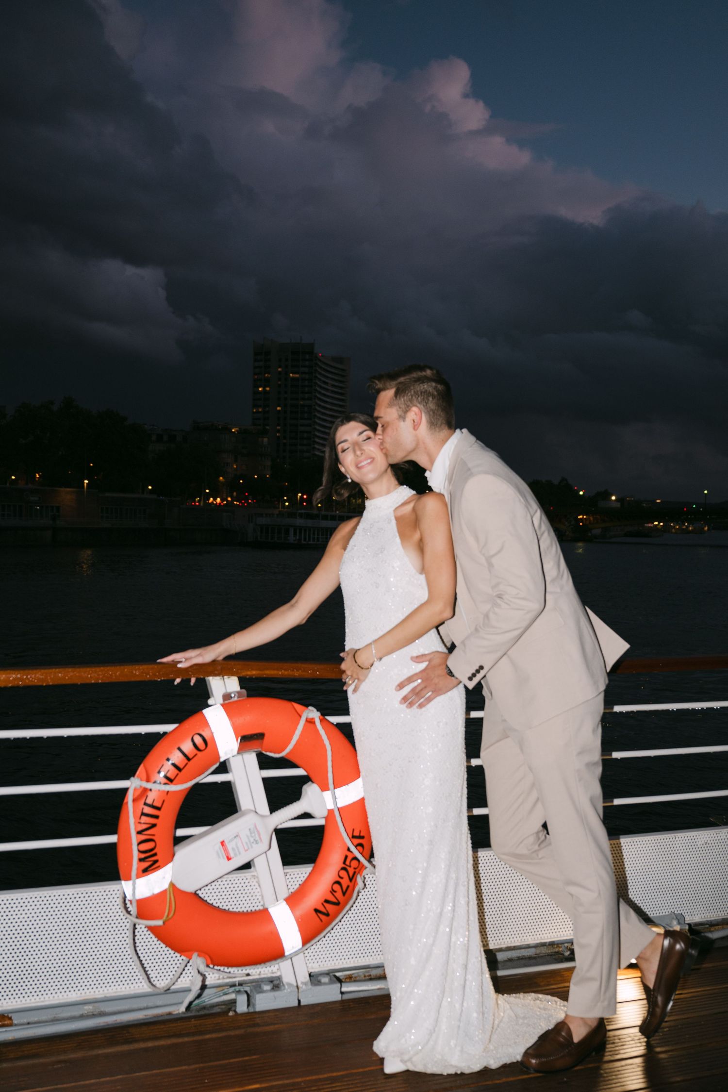 A bride and groom share a kiss on the deck of the Montebello boat at night in Paris.