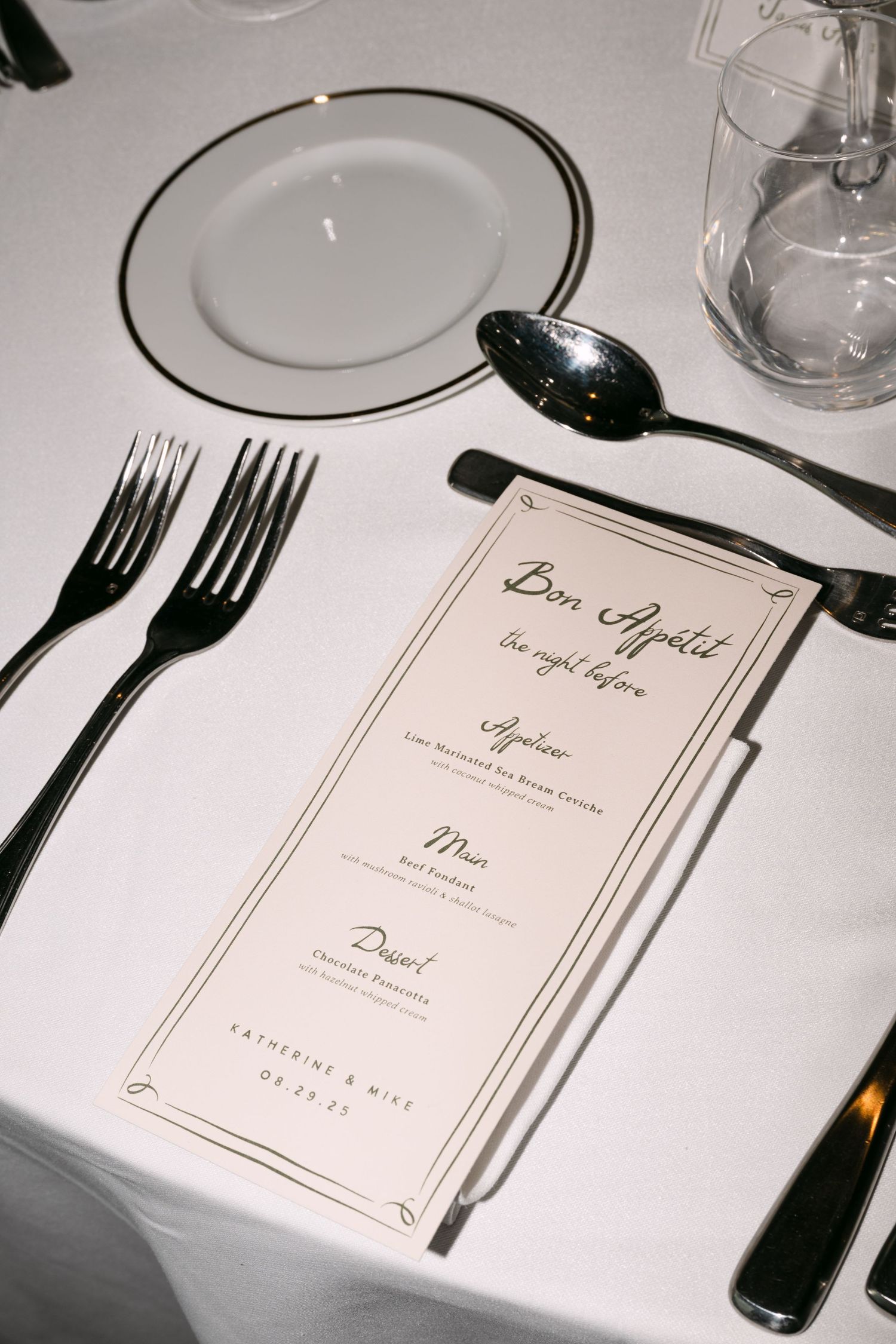Elegant wedding dinner menu card reading Bon Appetit placed on a white tablecloth with black cutlery.