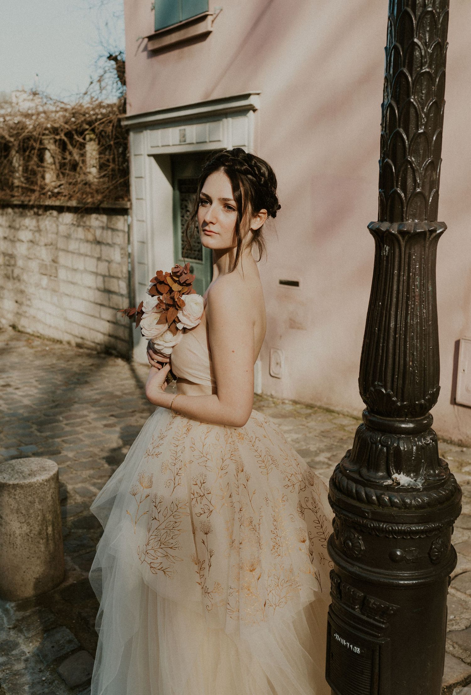 Dreamy bridal portrait with autumn flowers against pink wall and ornate lamppost.