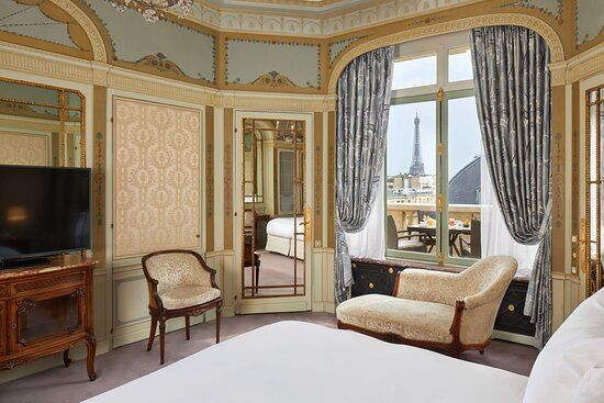 Luxurious hotel room with vintage decor, ornate moldings, and a window offering views of the Eiffel Tower in Paris.