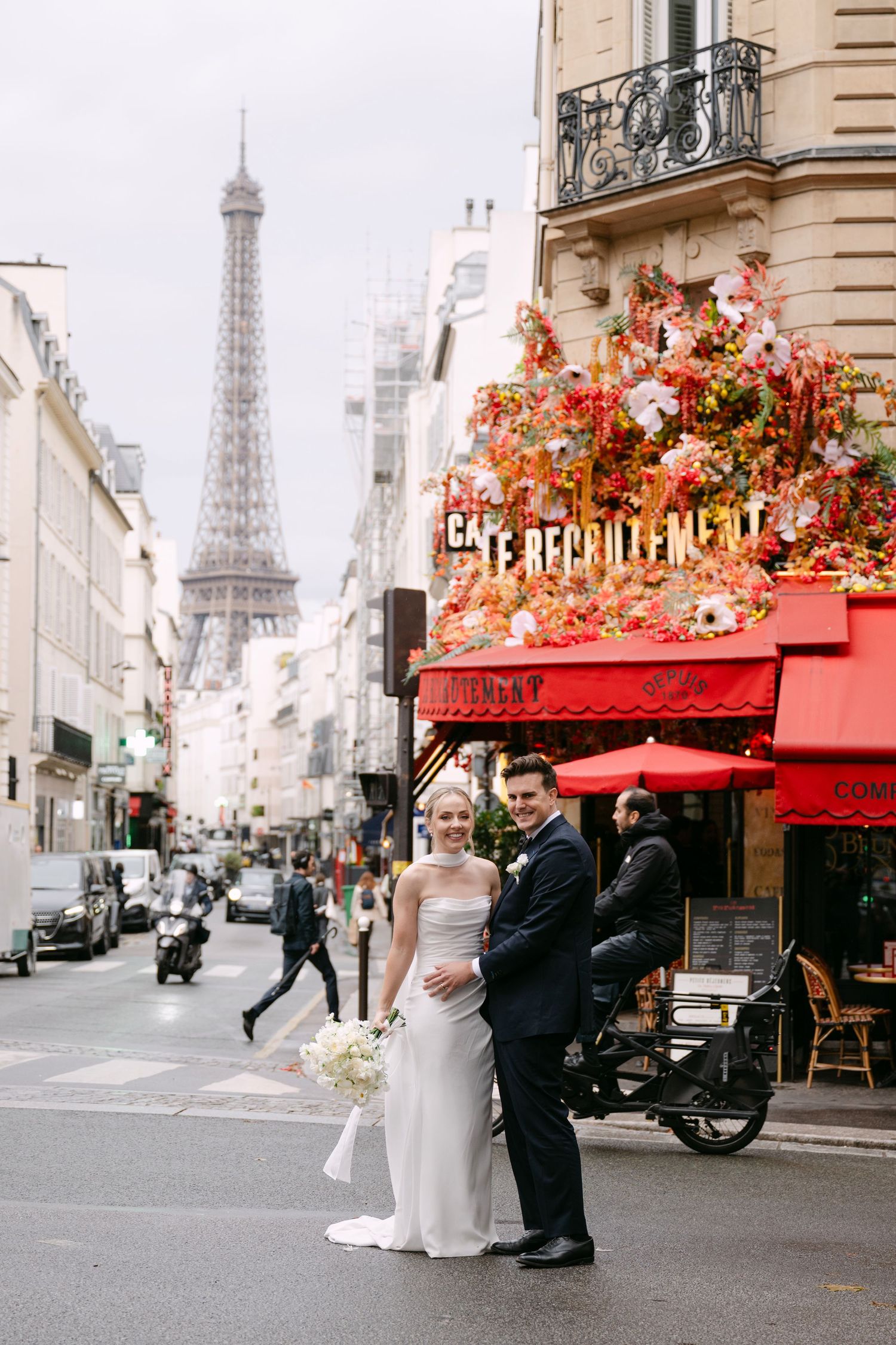 A couple poses on a charming Paris street with the iconic Eiffel Tower and red cafe awning in the background.
