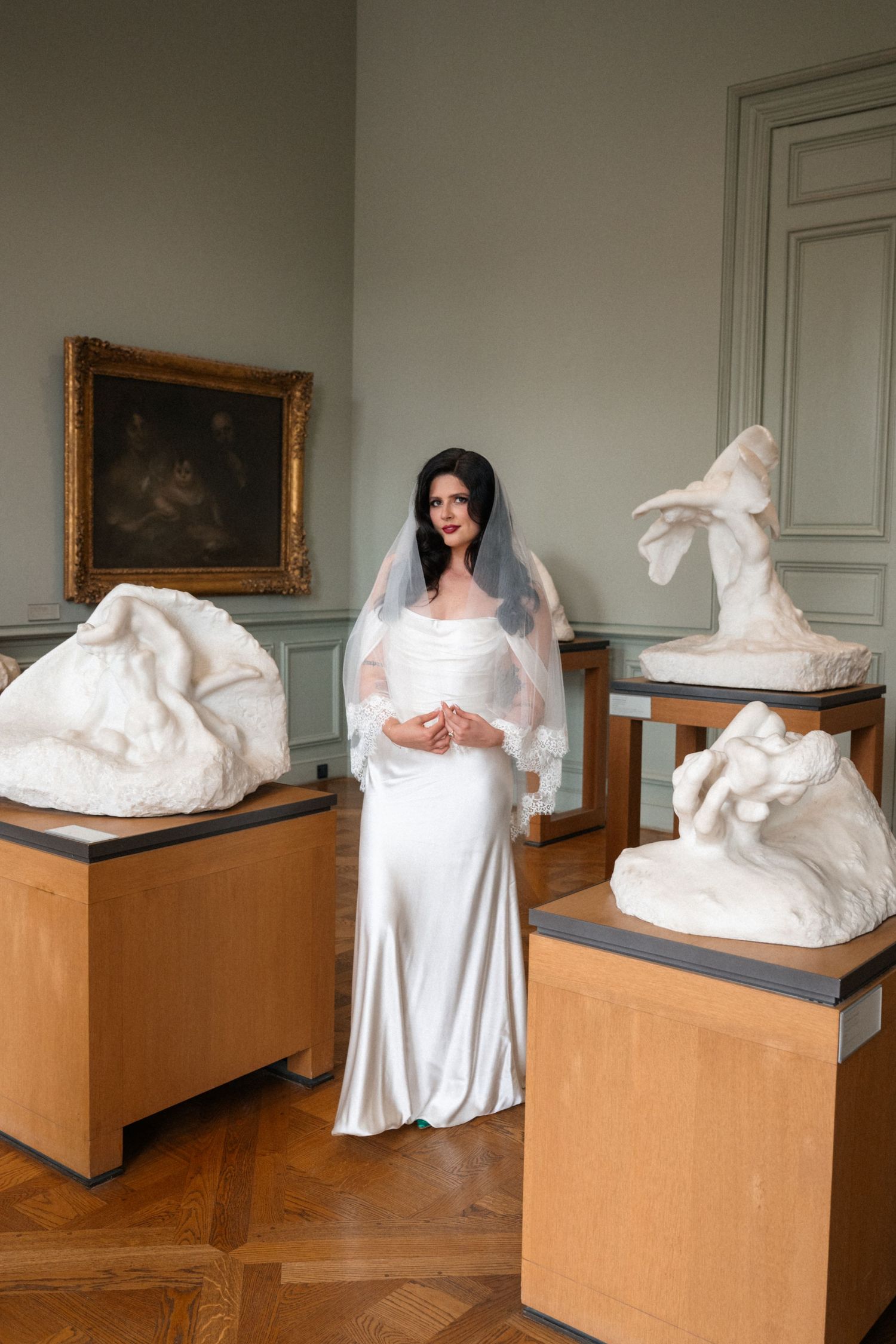 A series of white sculptural forms on wooden pedestals displayed in a gallery space with framed artwork on walls.