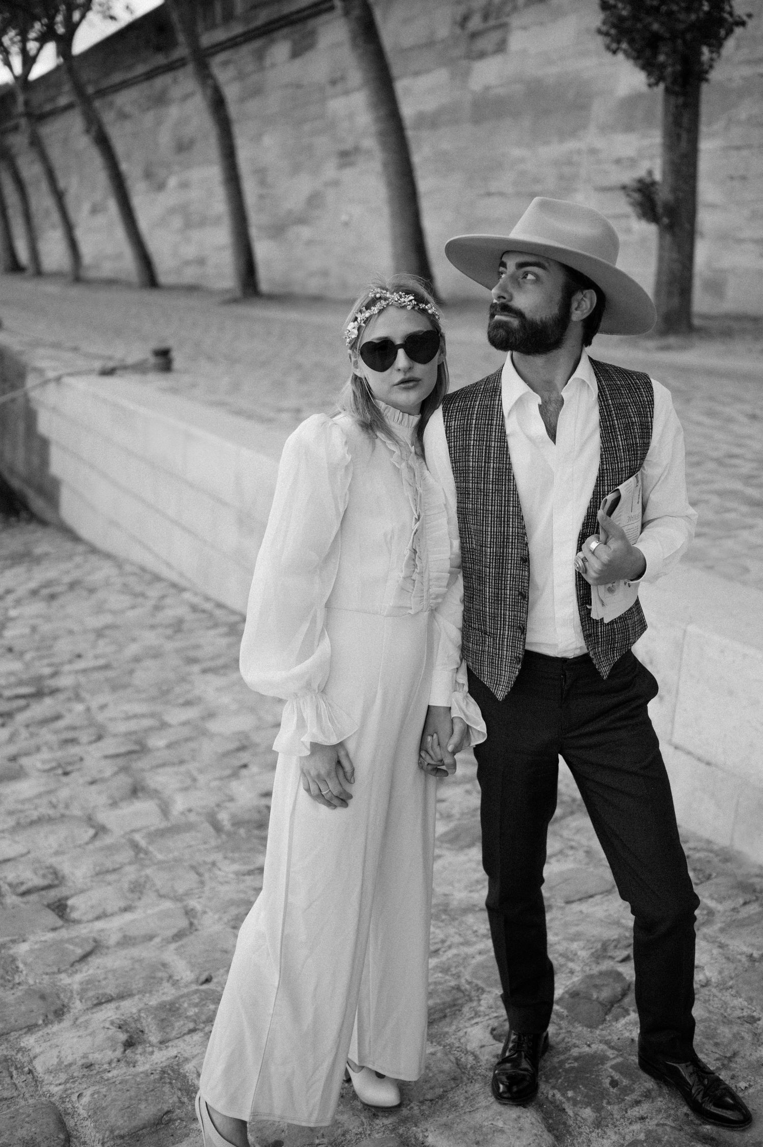 A full-length portrait of a couple in vintage-inspired wedding attire on a cobblestone street.