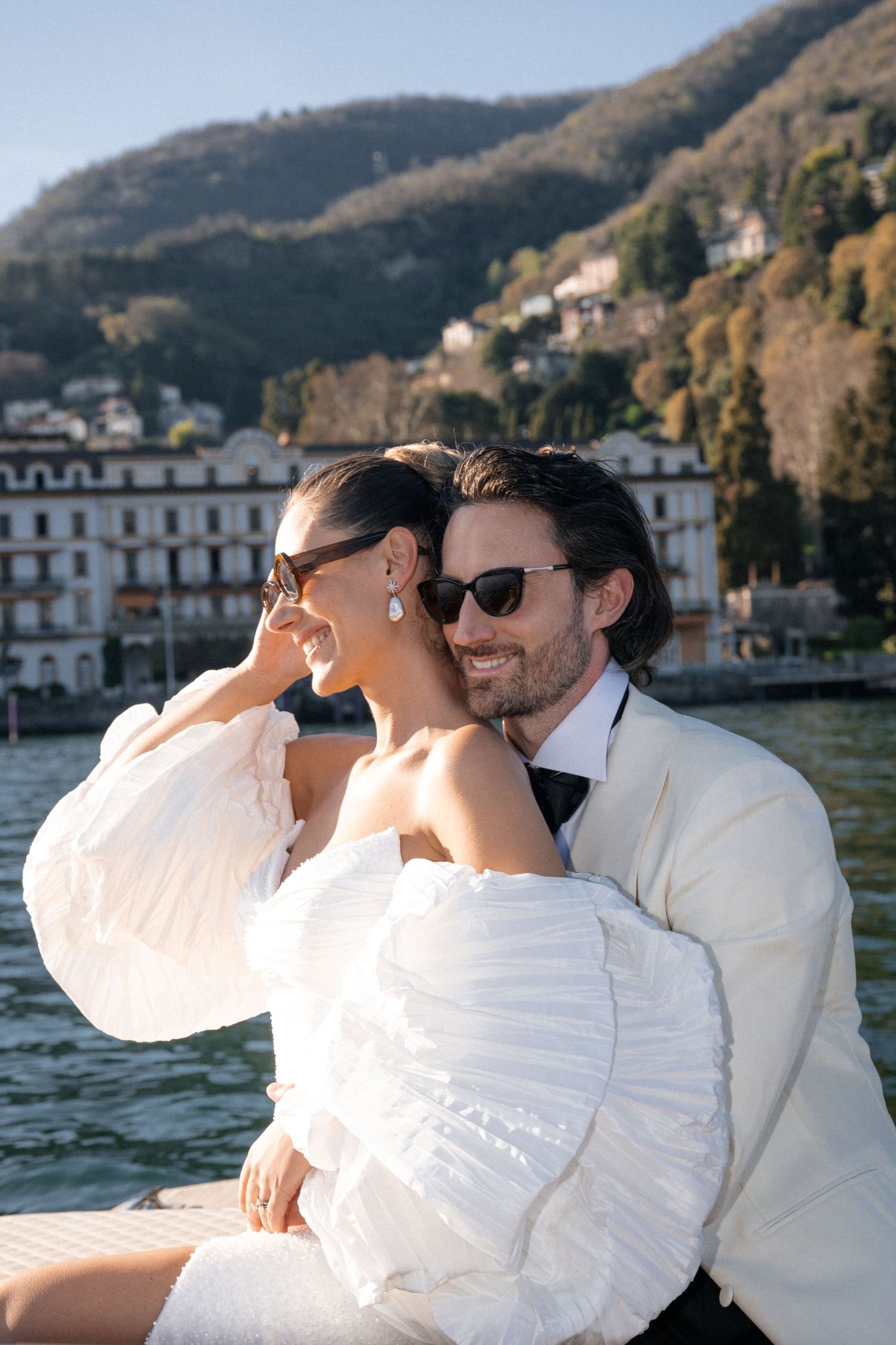 Smiling bride and groom in sunglasses sharing a tender moment on a boat at Lake Como.