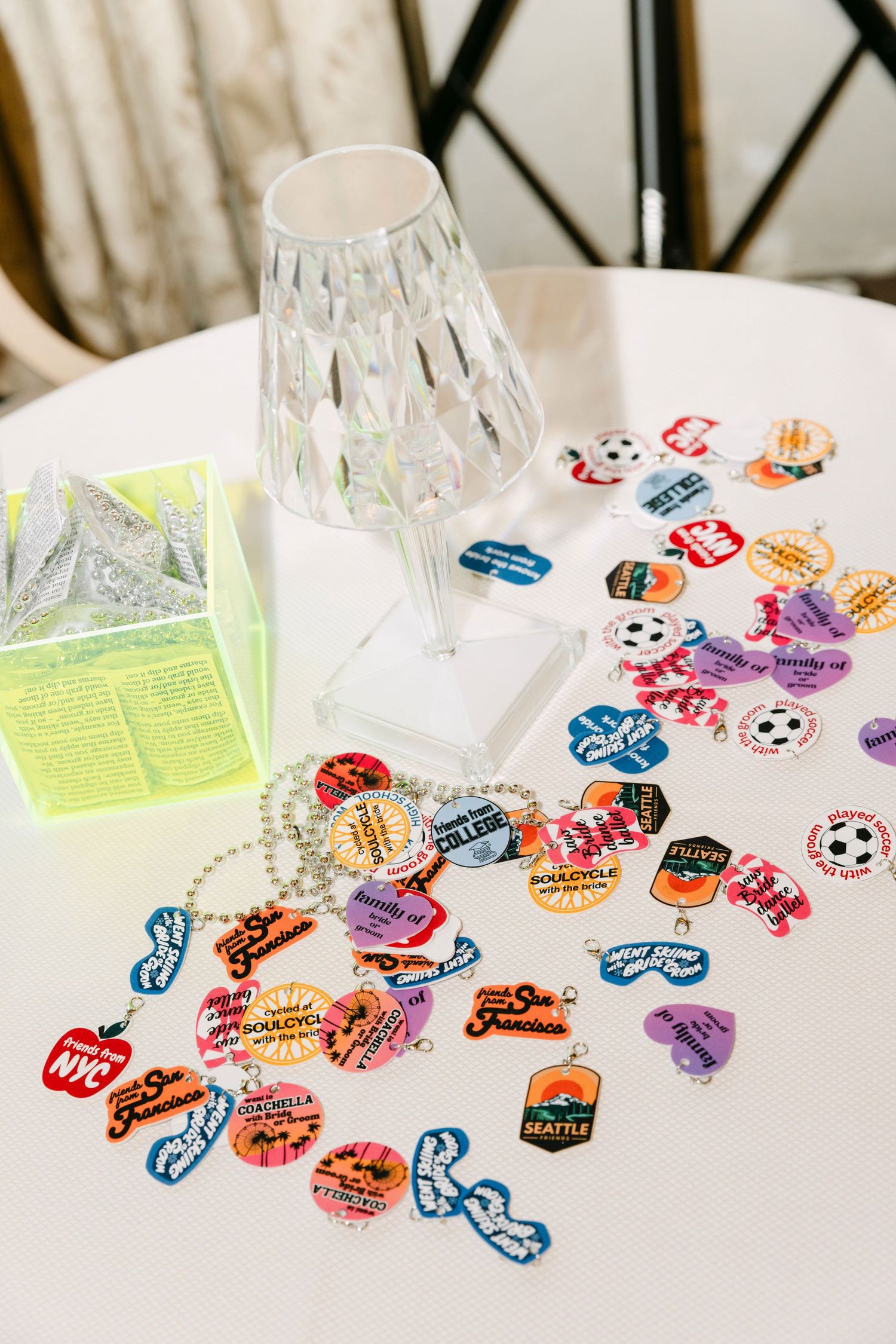 Colorful city-themed charm necklaces and stickers scattered on white table at wedding reception.