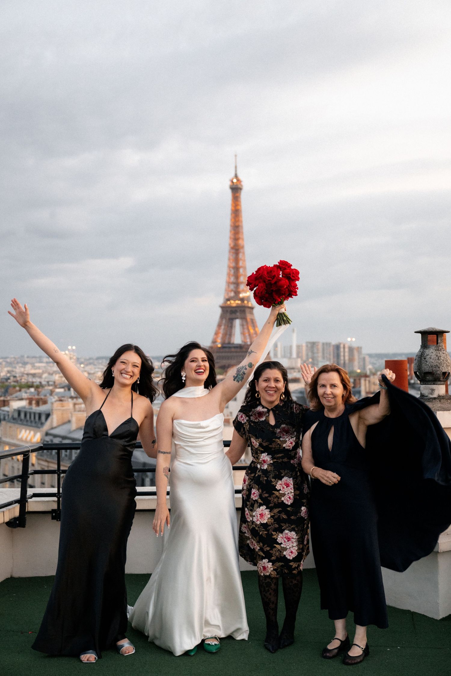 Bride and three female guests celebrating joyfully on Paris rooftop with Eiffel Tower in background.