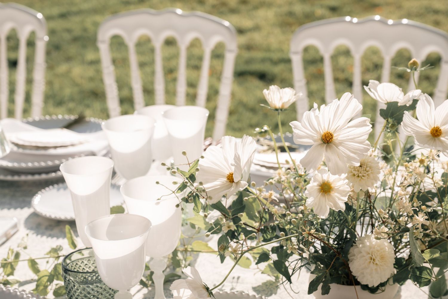 Close-up of white cosmos flowers and dahlia centerpiece on sunlit outdoor wedding table.