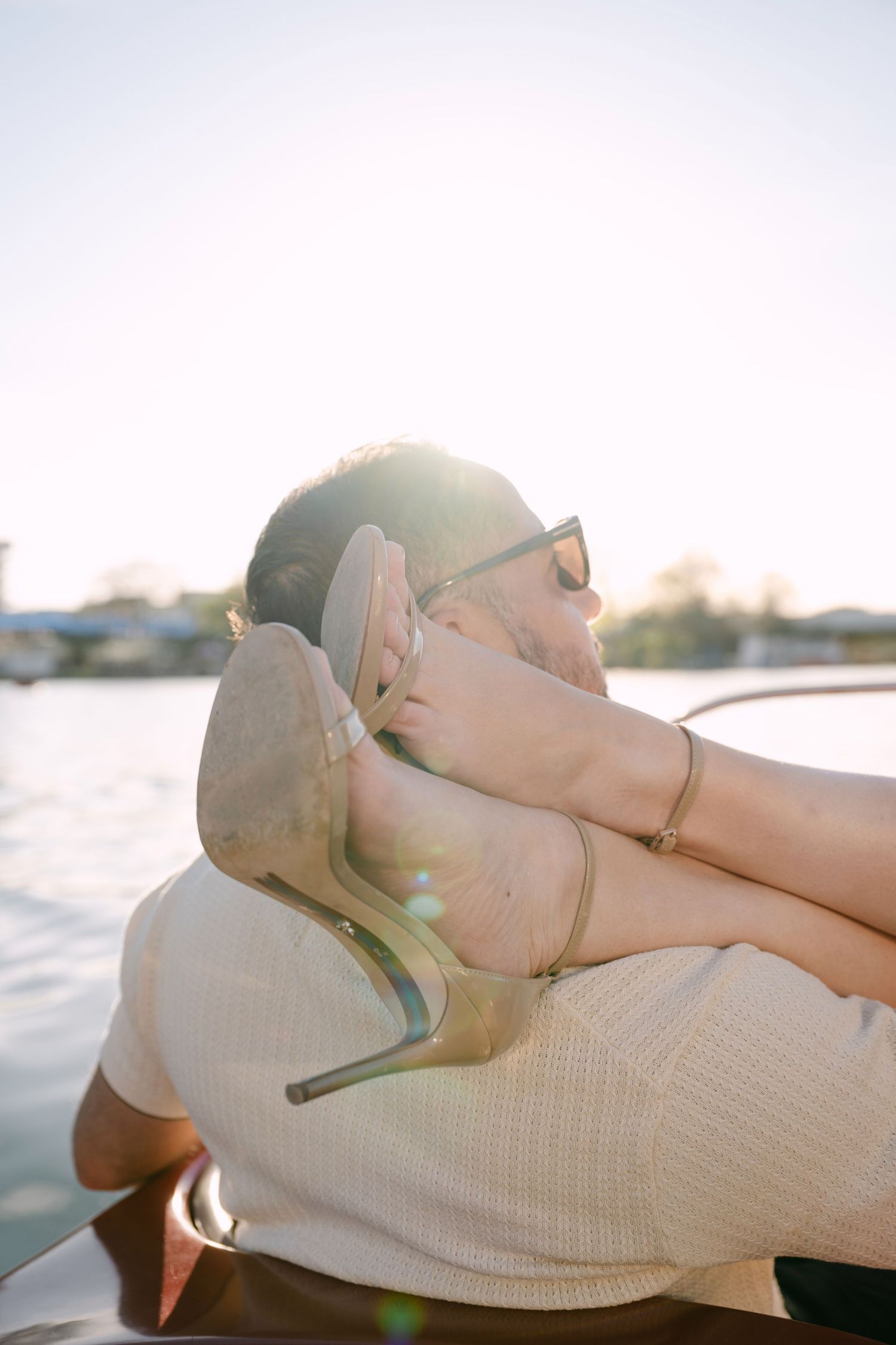 Couple enjoying a romantic boat ride at golden hour, woman's heels resting on man.