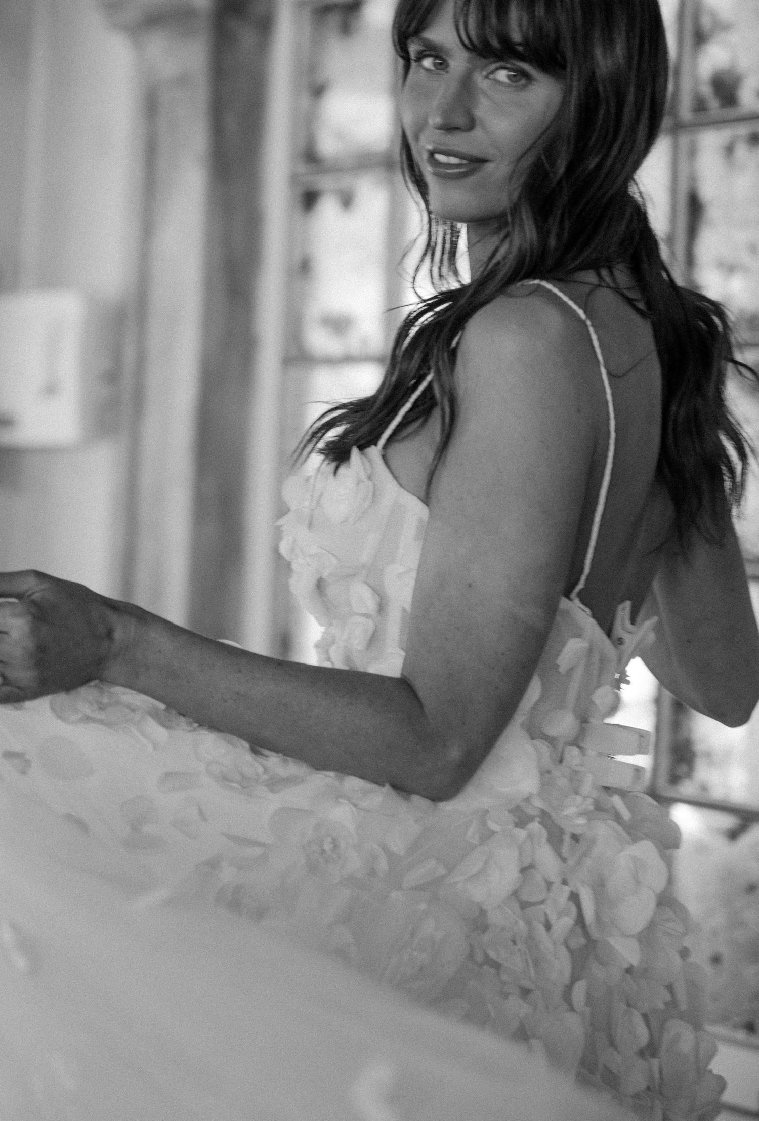 Black and white photo of a woman in a floral applique wedding gown with spaghetti straps, looking over her shoulder.