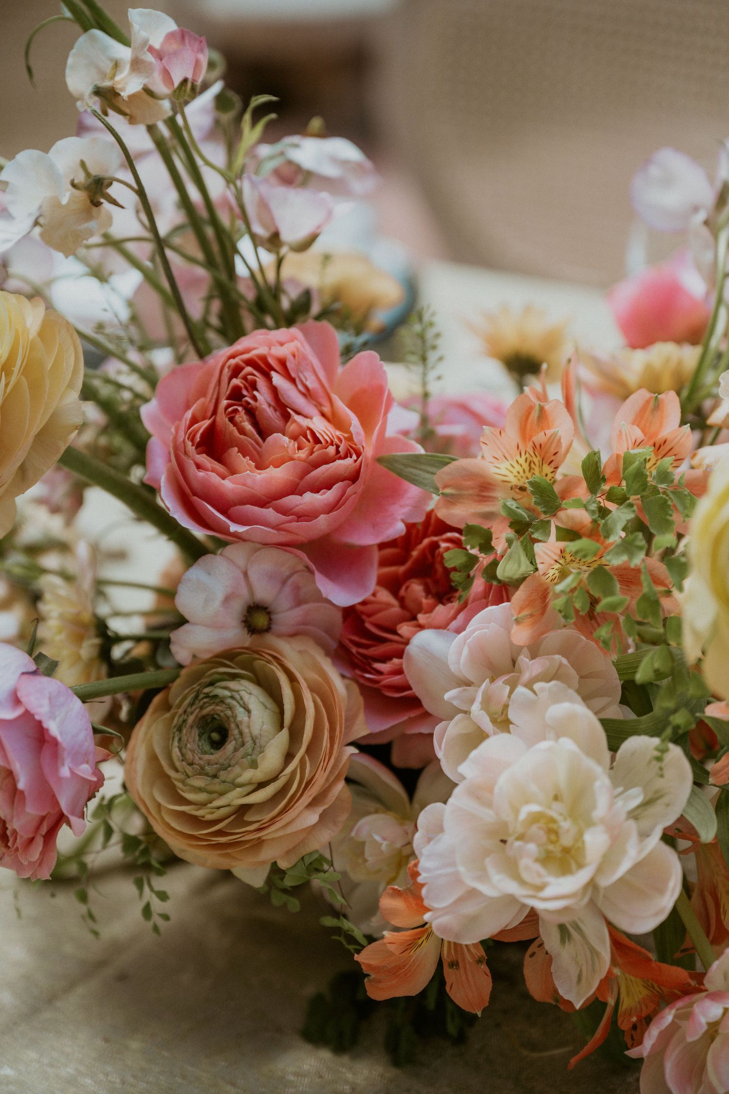 Lush wedding floral centerpiece featuring pink garden roses, ranunculus, and orange alstroemeria in warm blush tones.