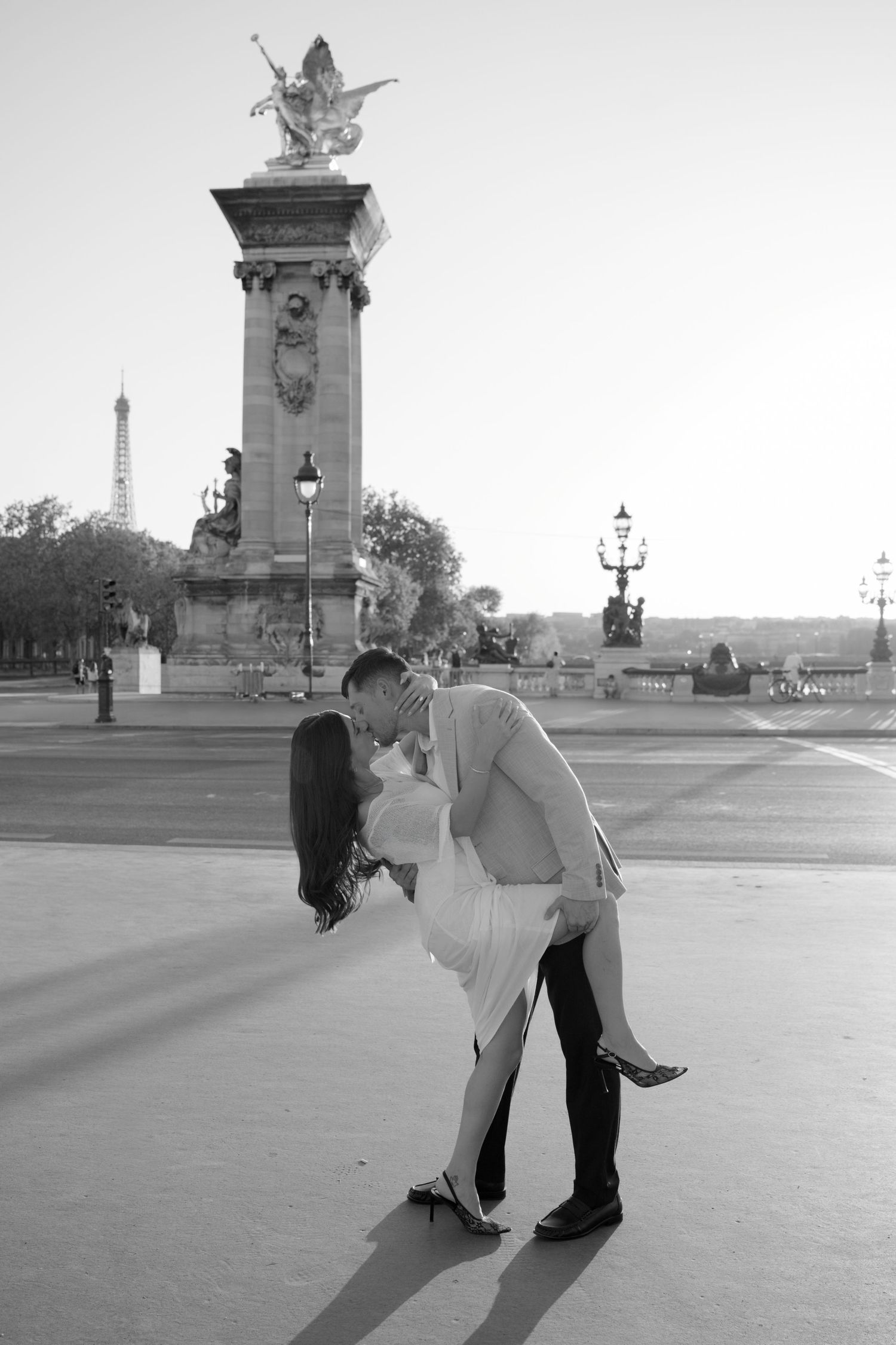 Couple sharing a romantic dip kiss on Pont Alexandre III bridge in Paris, with the Eiffel Tower in the background.