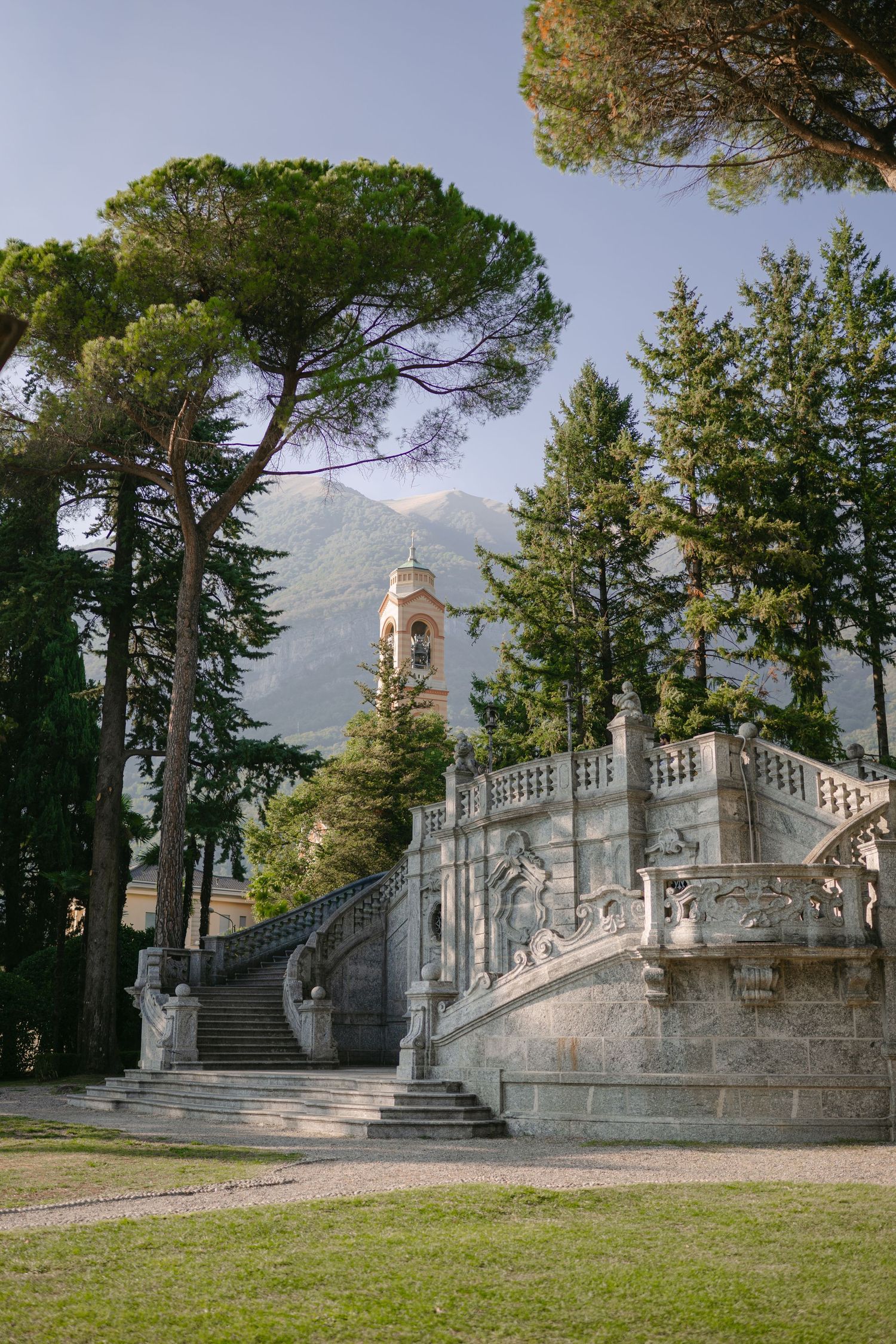 Elegant stone staircase with ornate balustrades surrounded by tall pine trees and mountain views at an Italian villa.