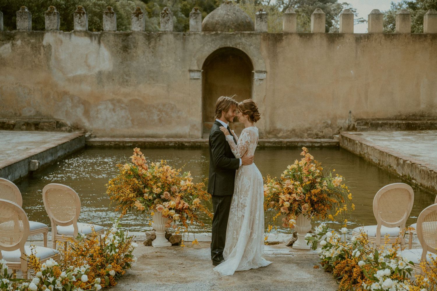 Couple celebrates wedding surrounded by yellow floral arrangements in stone courtyard.