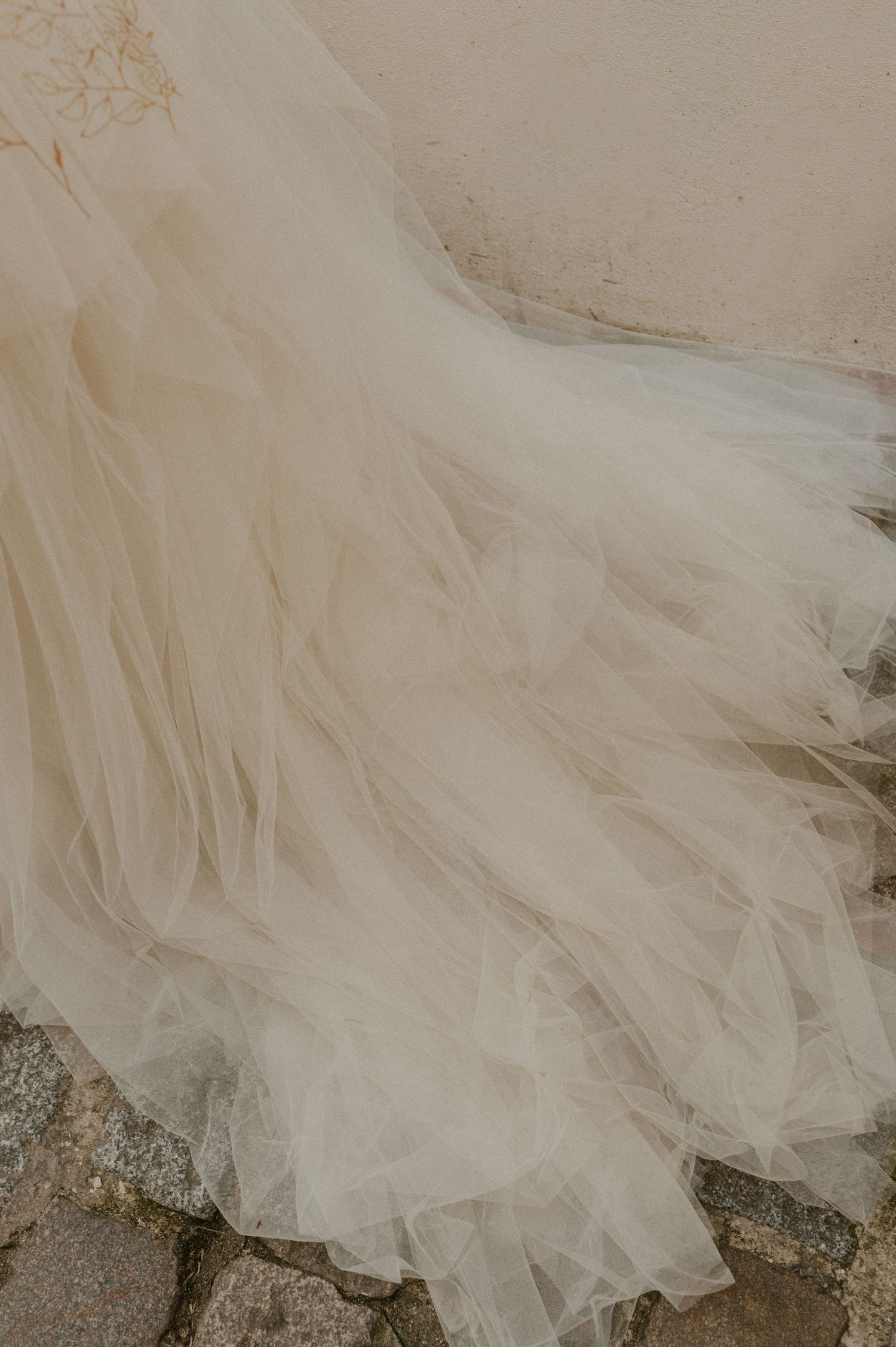 Close-up detail of flowing tulle wedding dress fabric trailing on cobblestone ground.