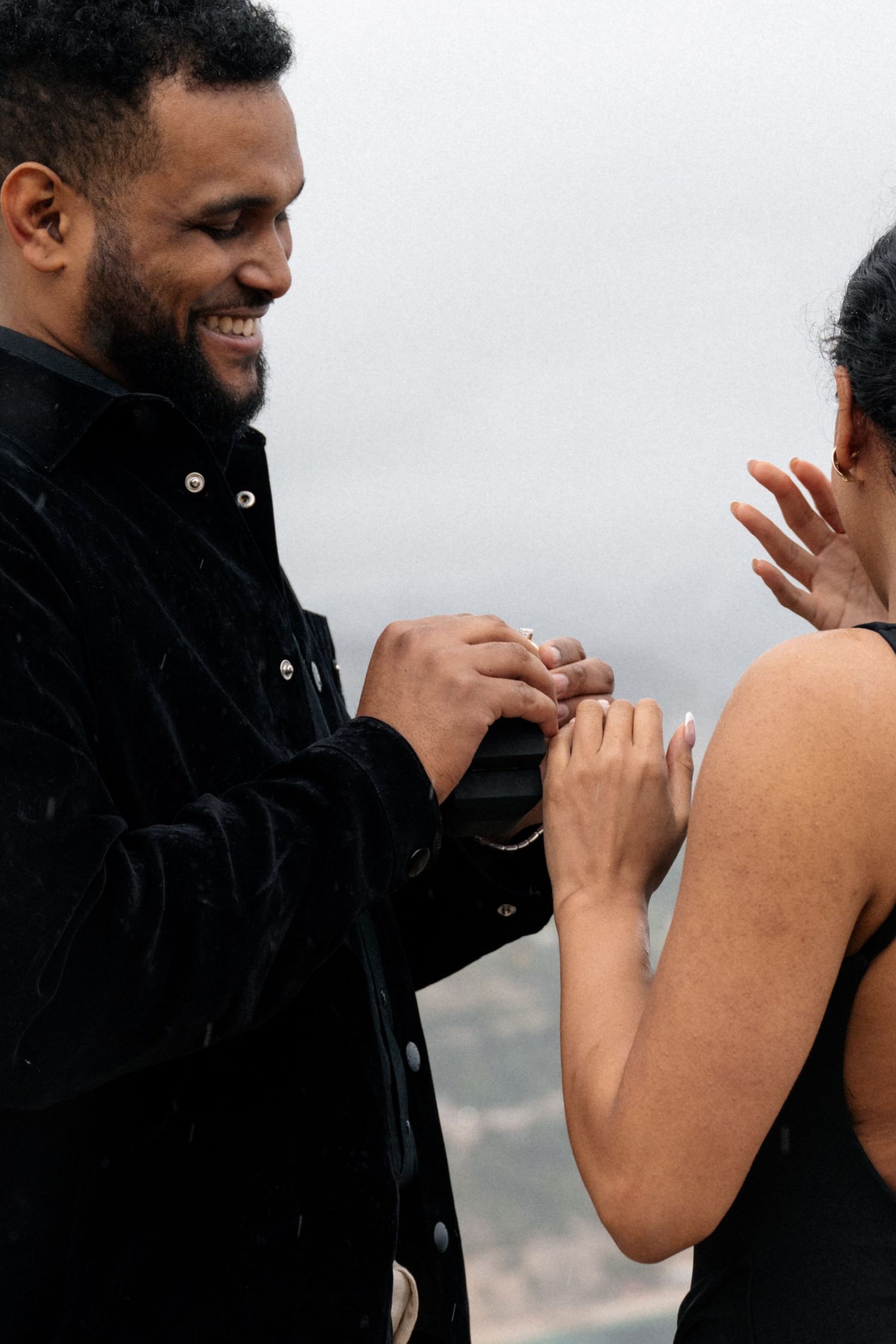 A couple shares a special engagement moment on a scenic cliffside overlooking a misty bay.