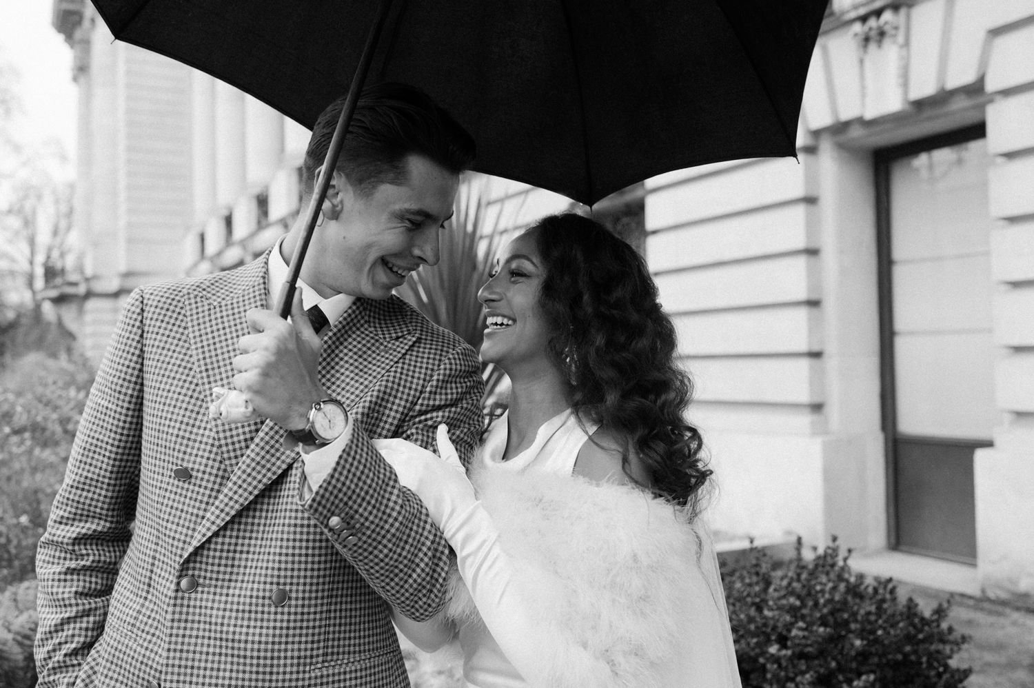 Candid black and white moment of a couple laughing while sharing an umbrella outdoors.