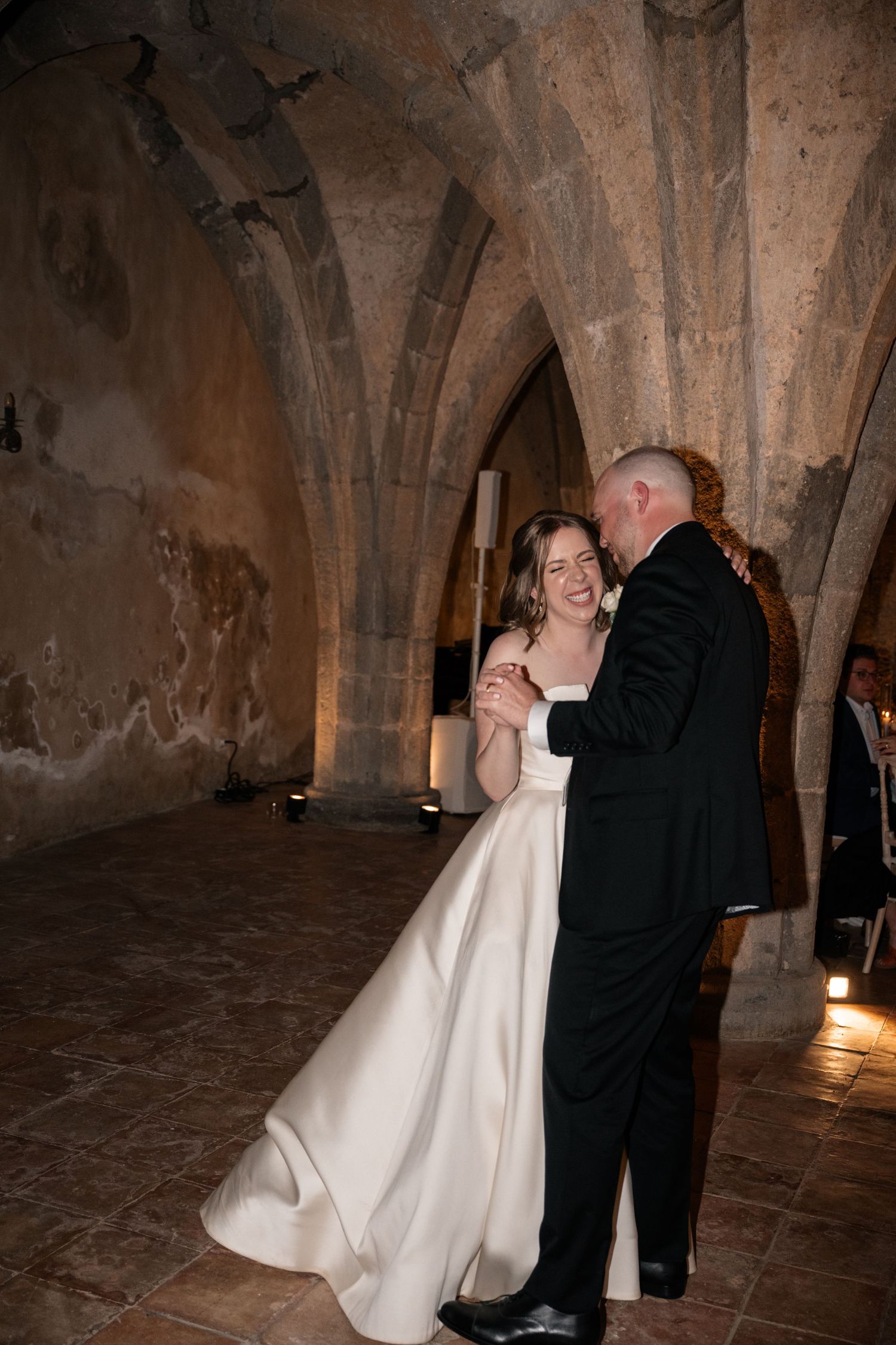 Bride and groom share their first dance in a romantic stone-vaulted medieval venue illuminated by warm candlelight.