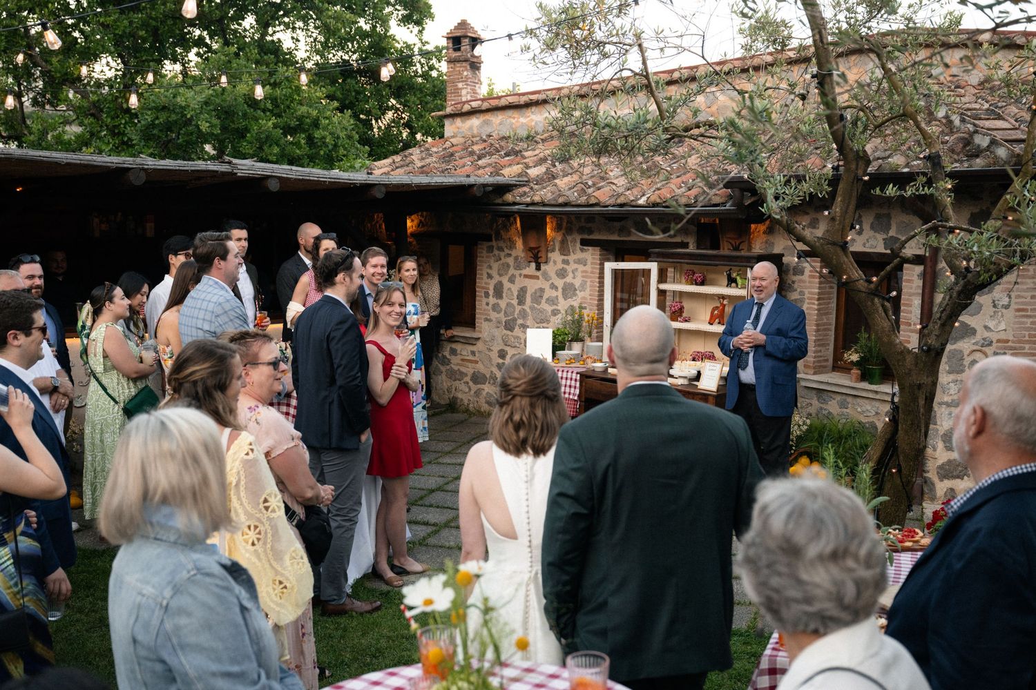 Wedding guests gathering outdoors in a rustic stone courtyard during an evening reception celebration.